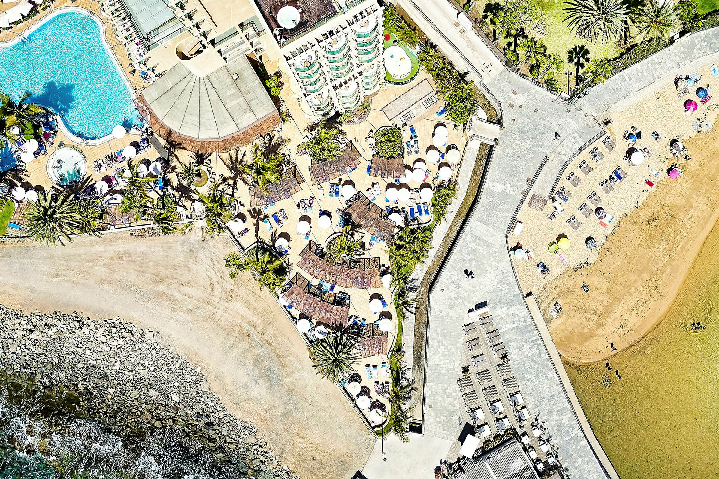 Luftfoto av et feriested med svømmebassenger, solsenger og parasoller nær stranden. (AI-generert tekst)