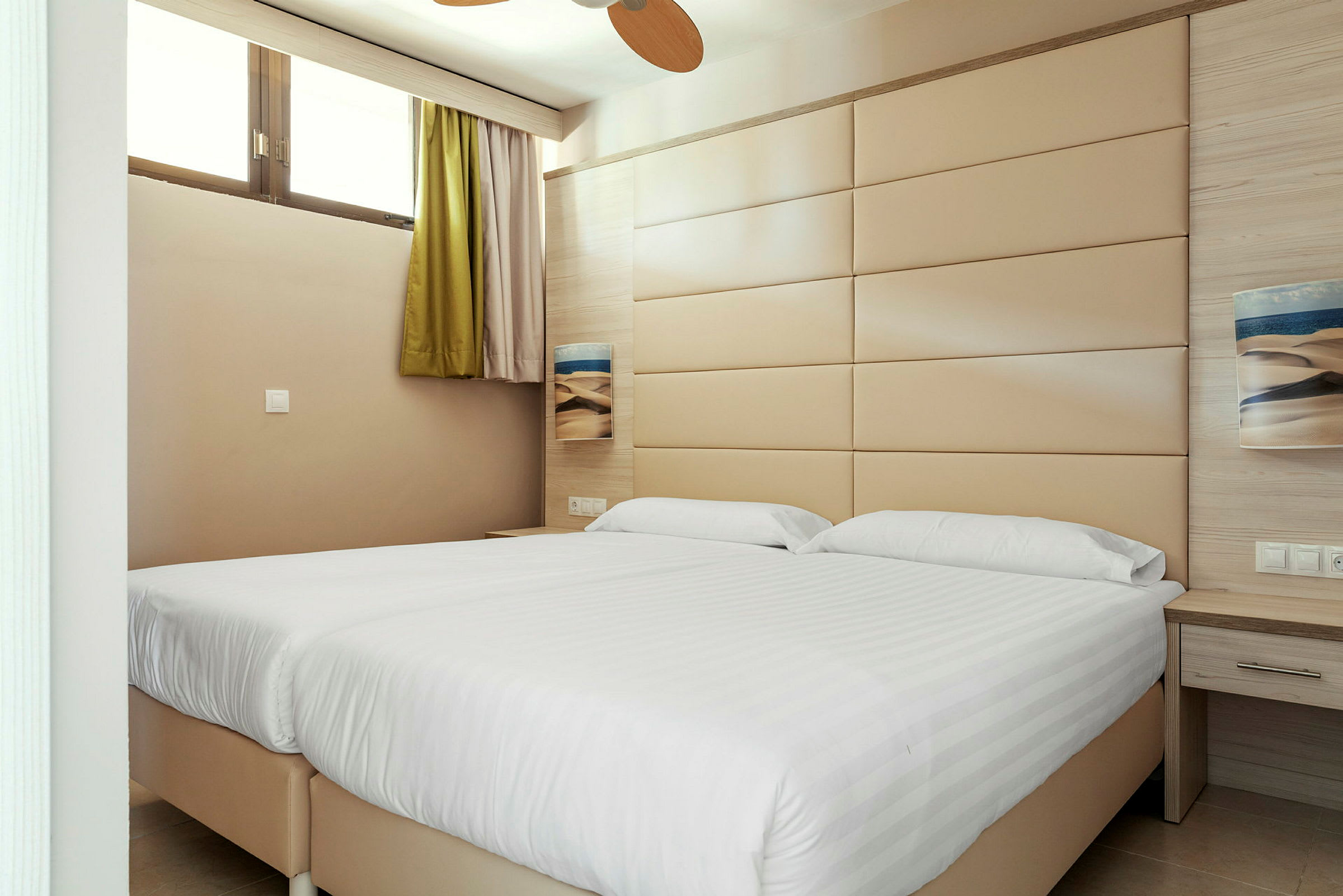Et hotellrom med to senger og en beige veggpanel. (AI-generert tekst)