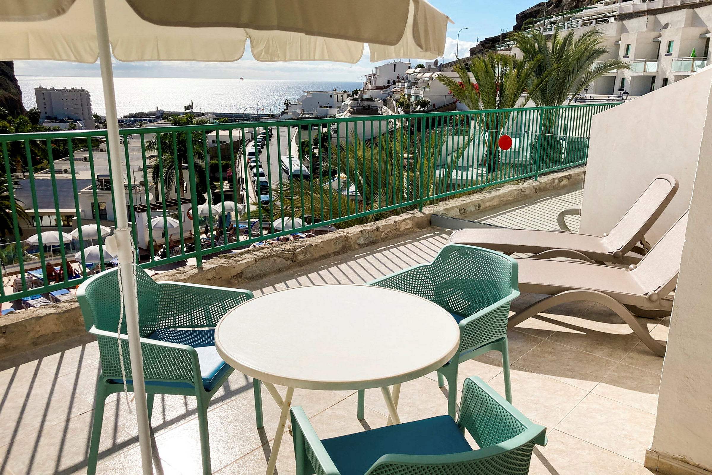 Terrasse med et rundt bord, stoler og solsenger, havutsikt i bakgrunnen. (AI-generert tekst)