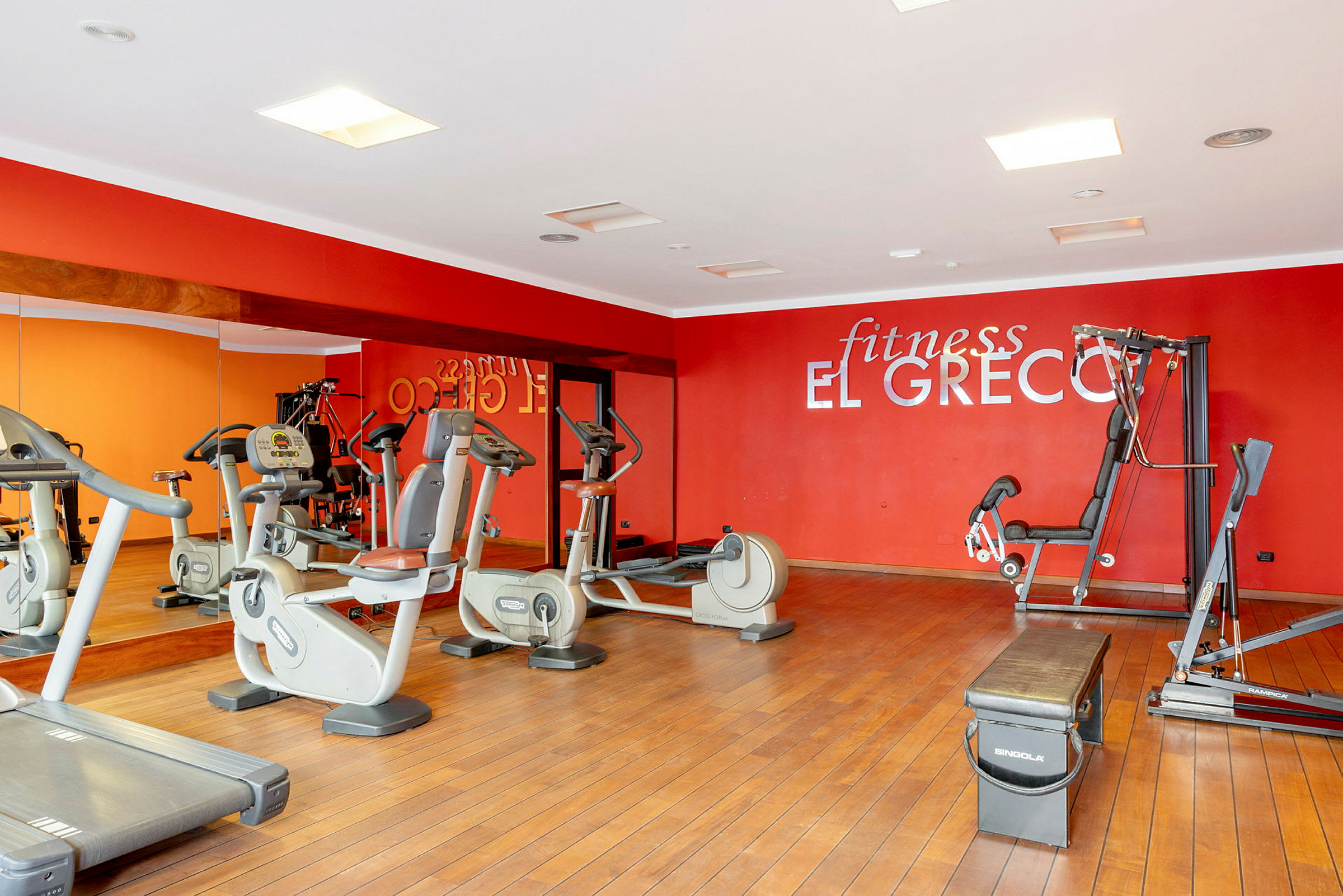 Et treningsstudio med treningsapparater, speil og en rød vegg med teksten 'fitness El Greco'. (AI-generert tekst)