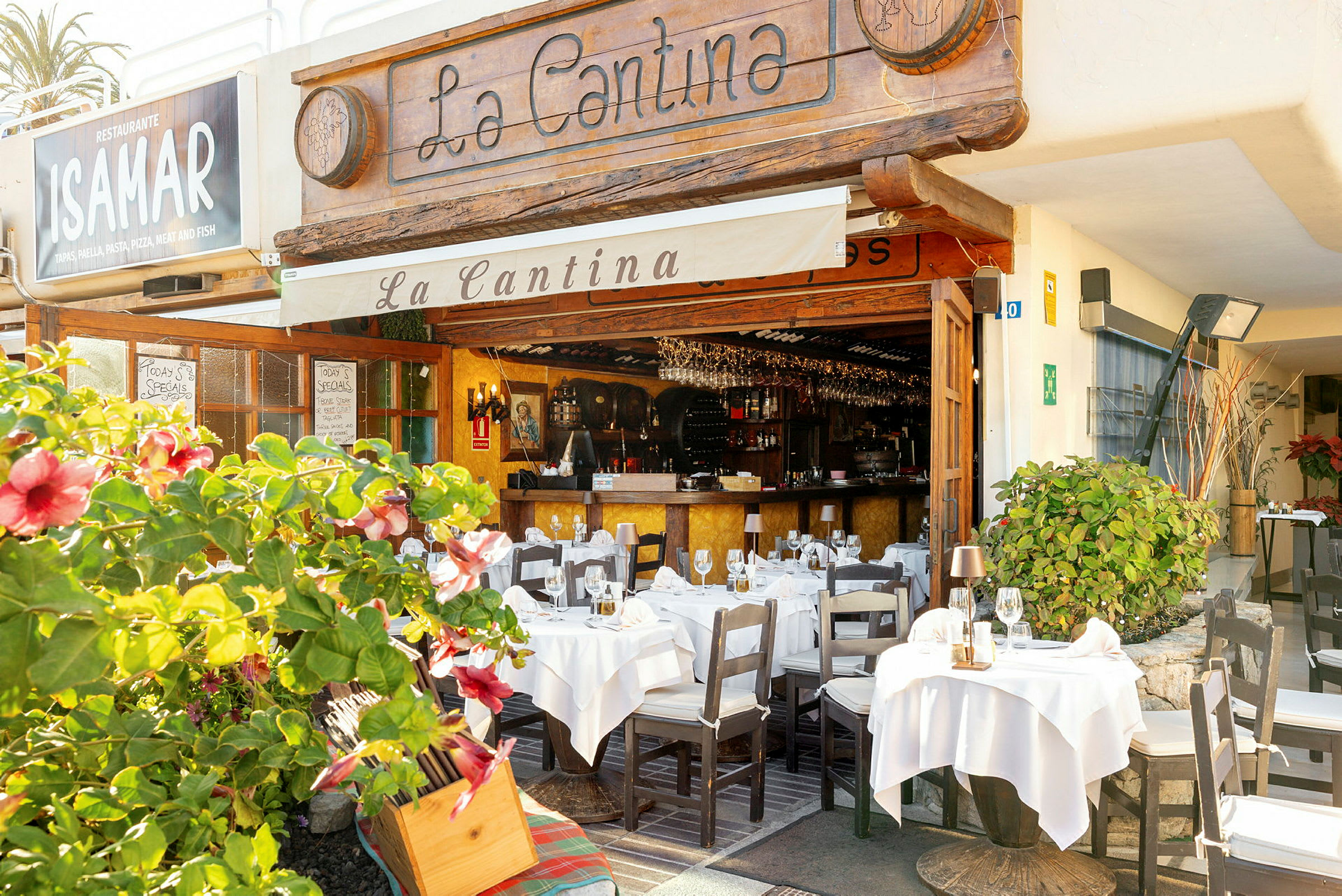 En restaurant med uteservering dekorert med hvite duker og blomstrende planter. (AI-generert tekst)