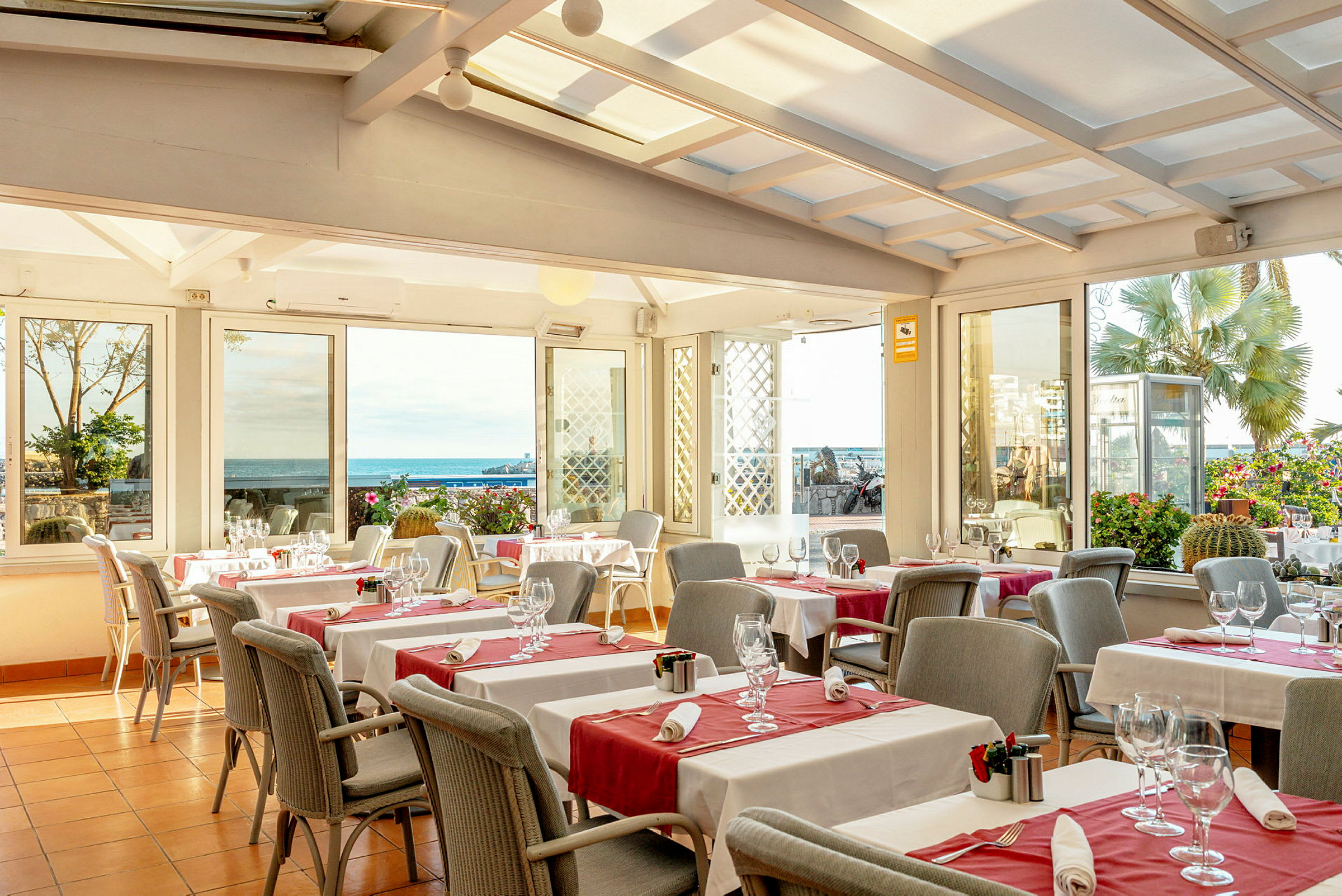 En restaurant med dekkede bord og glass med utsikt mot havet. (AI-generert tekst)