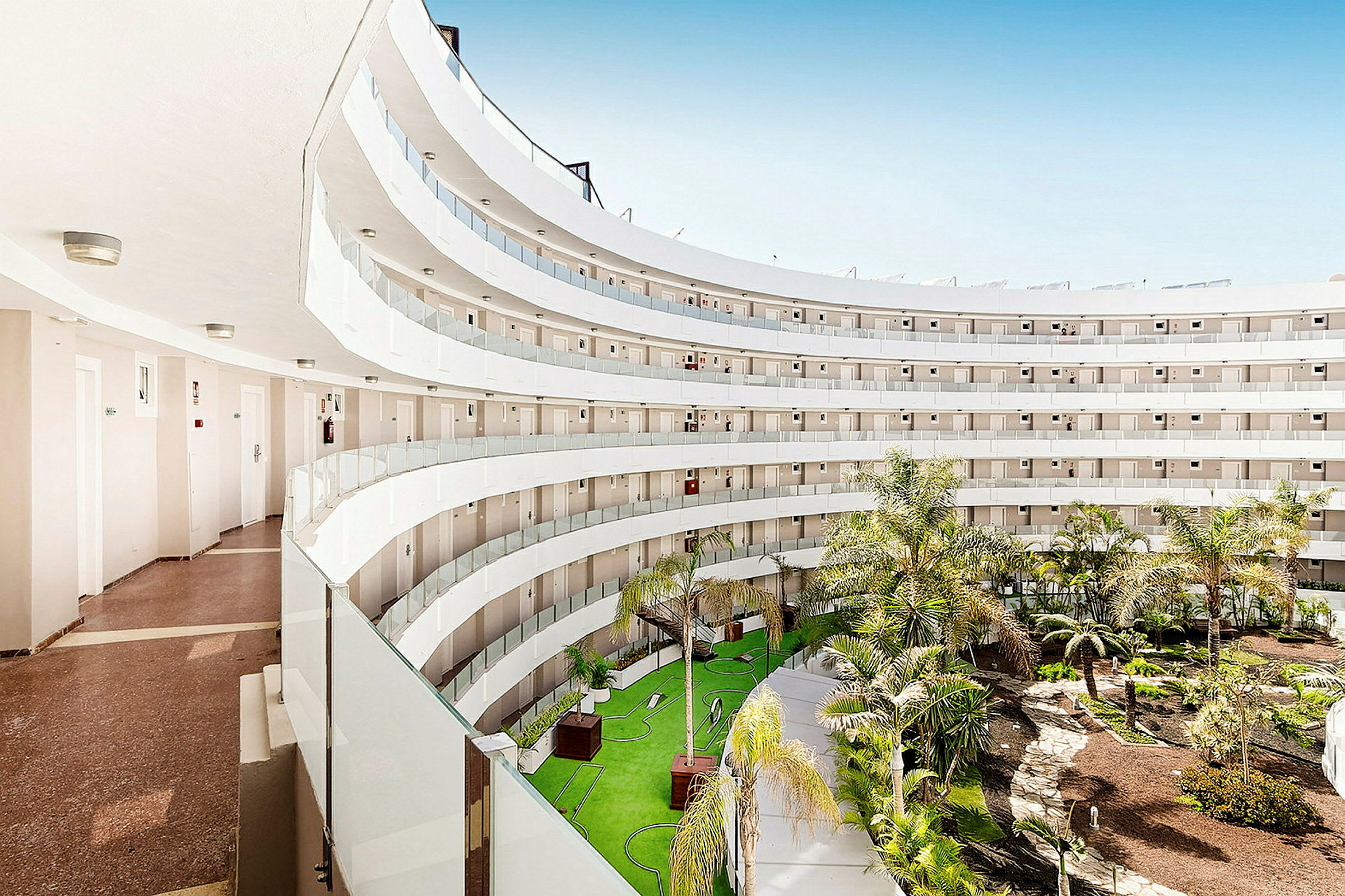 Bilde av en hotellbygning med flere etasjer som omgir en frodig indre gårdsplass. (AI-generert tekst)