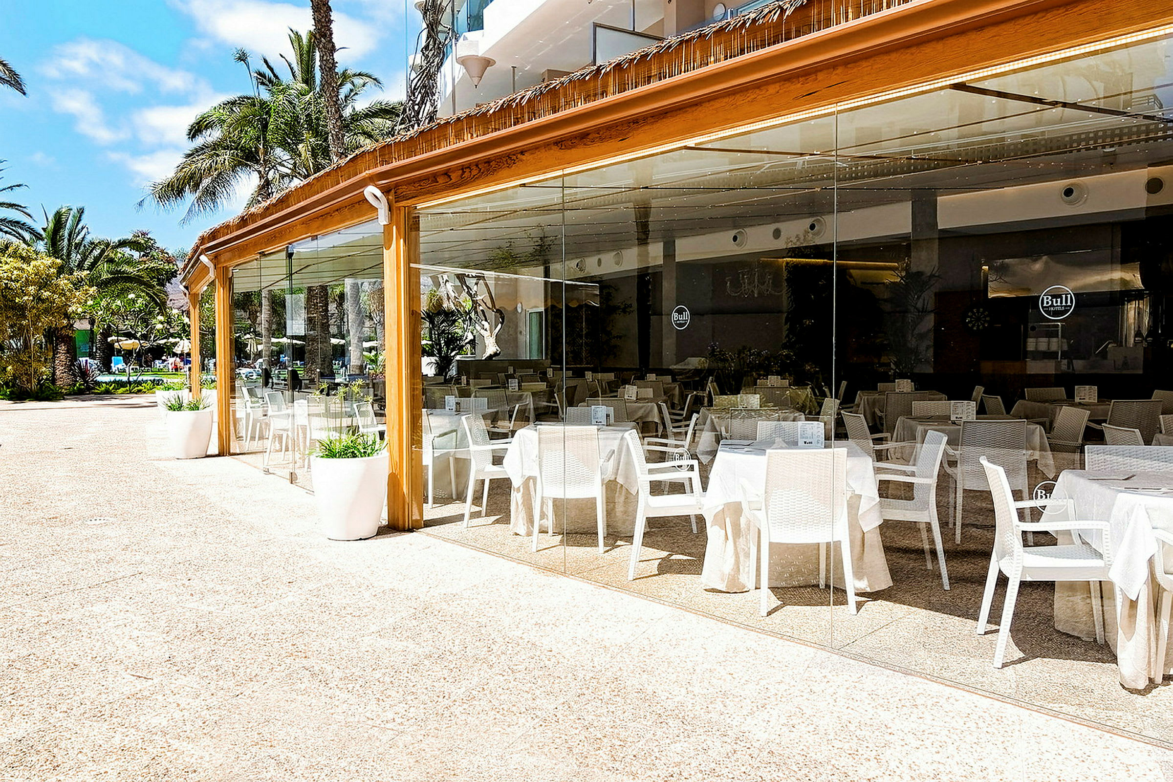 Bildet viser en utendørs restaurant med sitteplasser innelukket i glass. (AI-generert tekst)