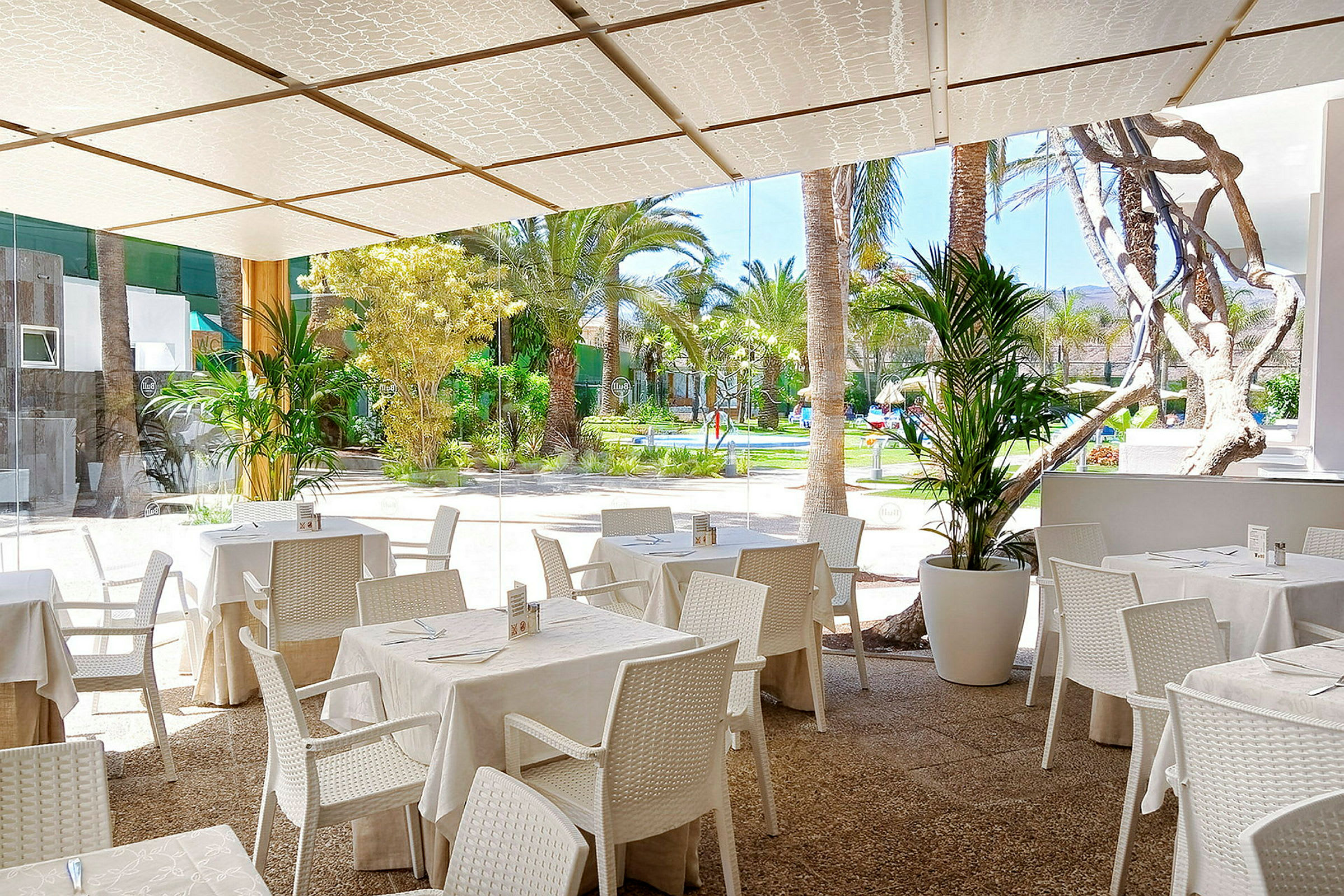 Utendørsrestaurant med hvite bord og stoler, samt utsikt over en frodig hage. (AI-generert tekst)