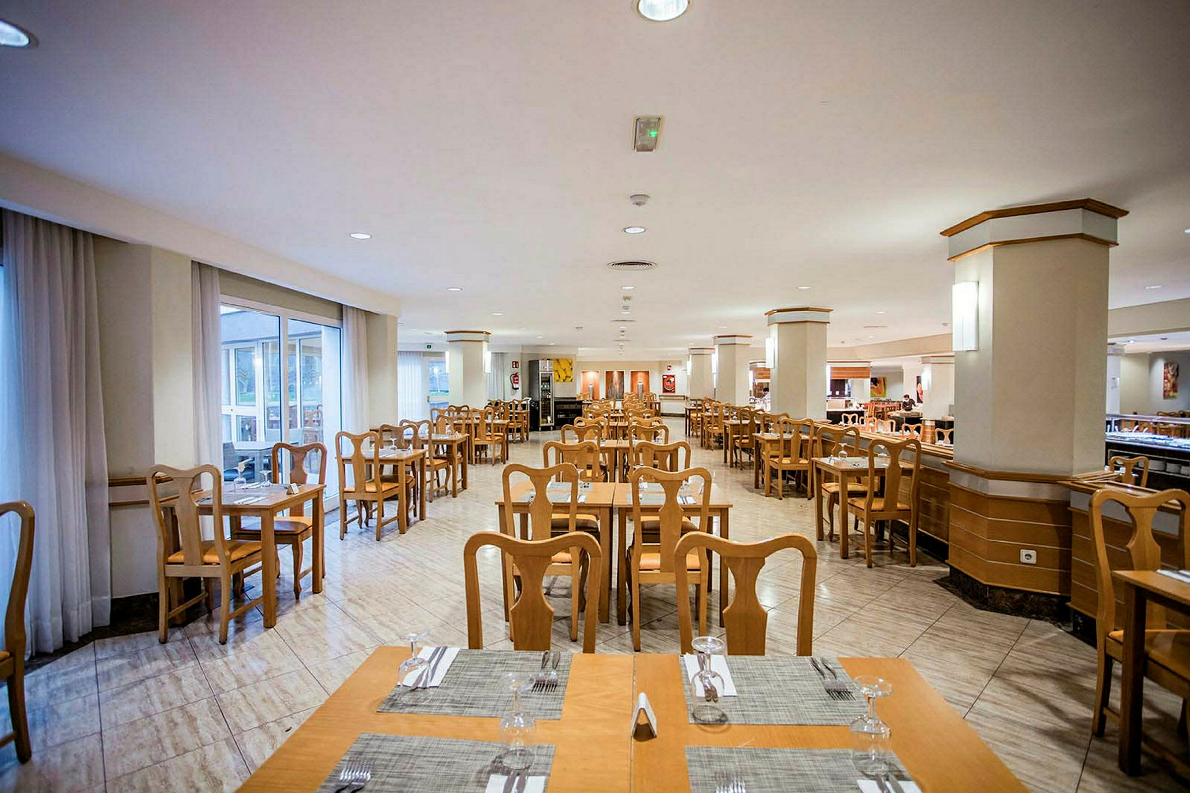 Restaurant med bord og stoler i tre samt duker og glass. (AI-generert tekst)