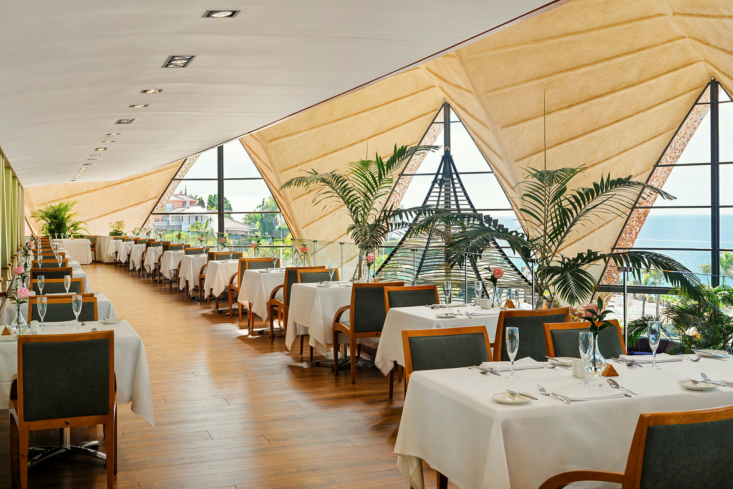 En elegant restaurant med bord dekket med hvite duker, store vinduer og frodige planter. (AI-generert tekst)