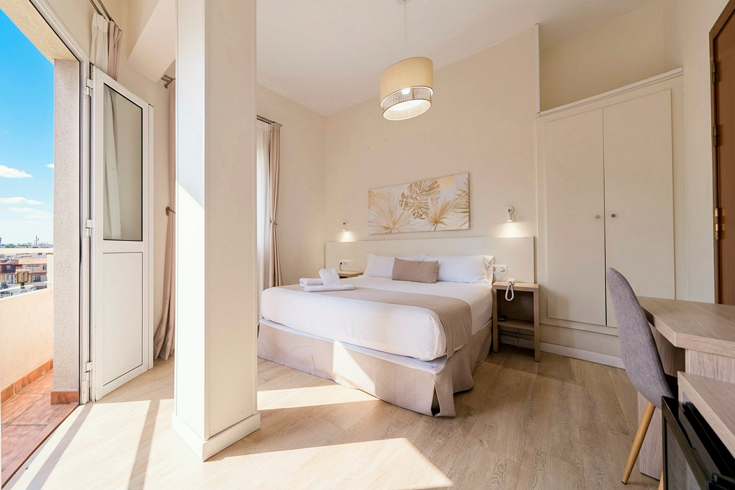Et hotellrom med en dobbeltseng, nattbord, skrivebord og garderobe, samt en balkong med utsikt. (AI-generert tekst)