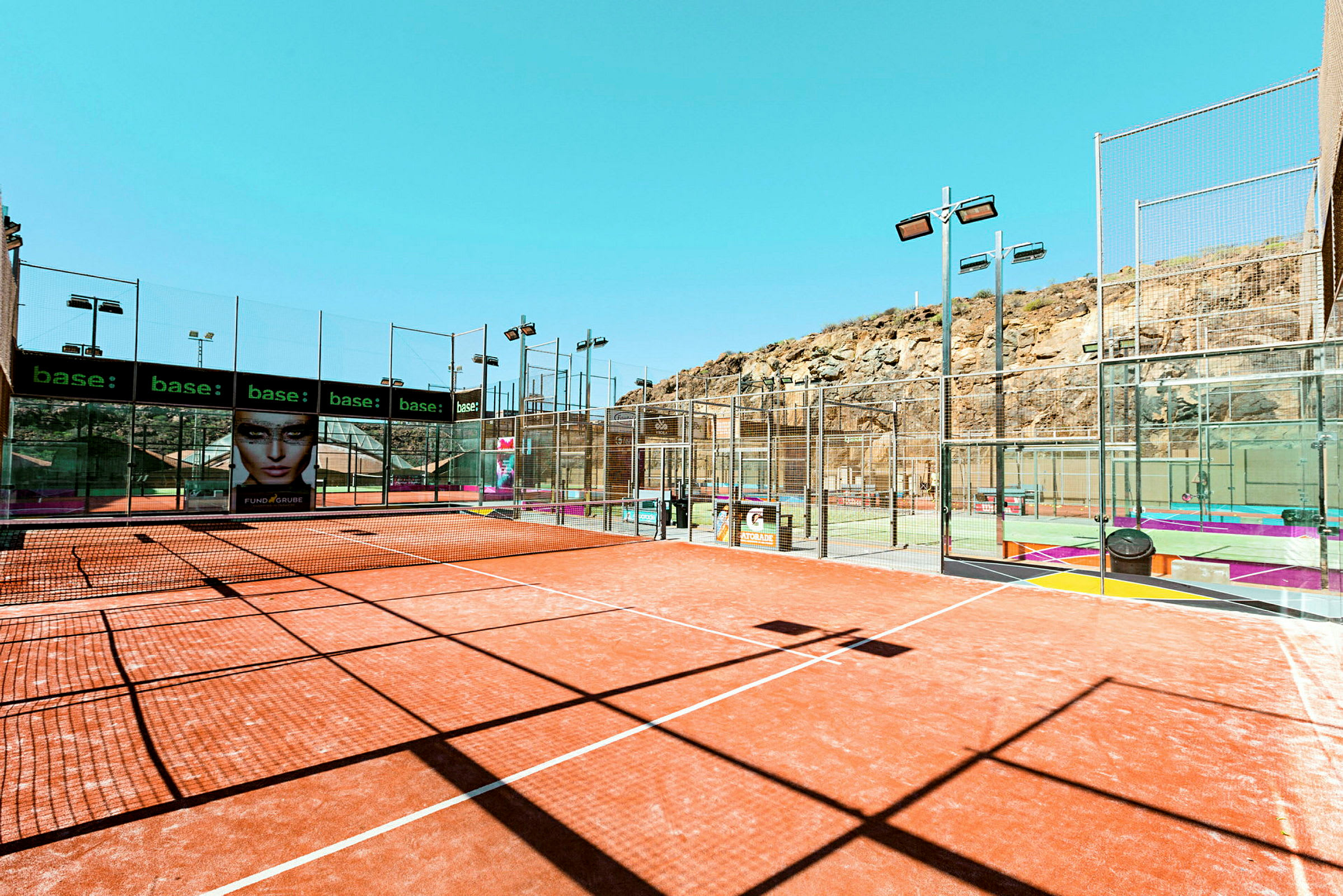 Utendørs padelbaner ved fjellterreng med nett og omkringliggende gjerder. (AI-generert tekst)