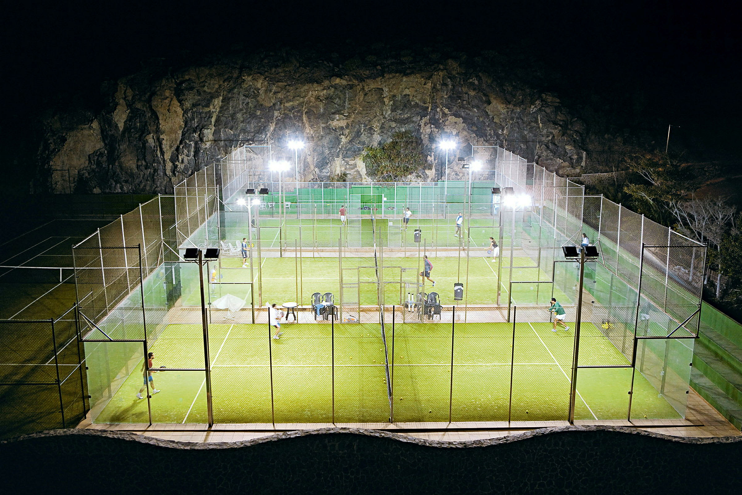 Utendørs padelbaner opplyst om kvelden, spillere synlige på banen. (AI-generert tekst)