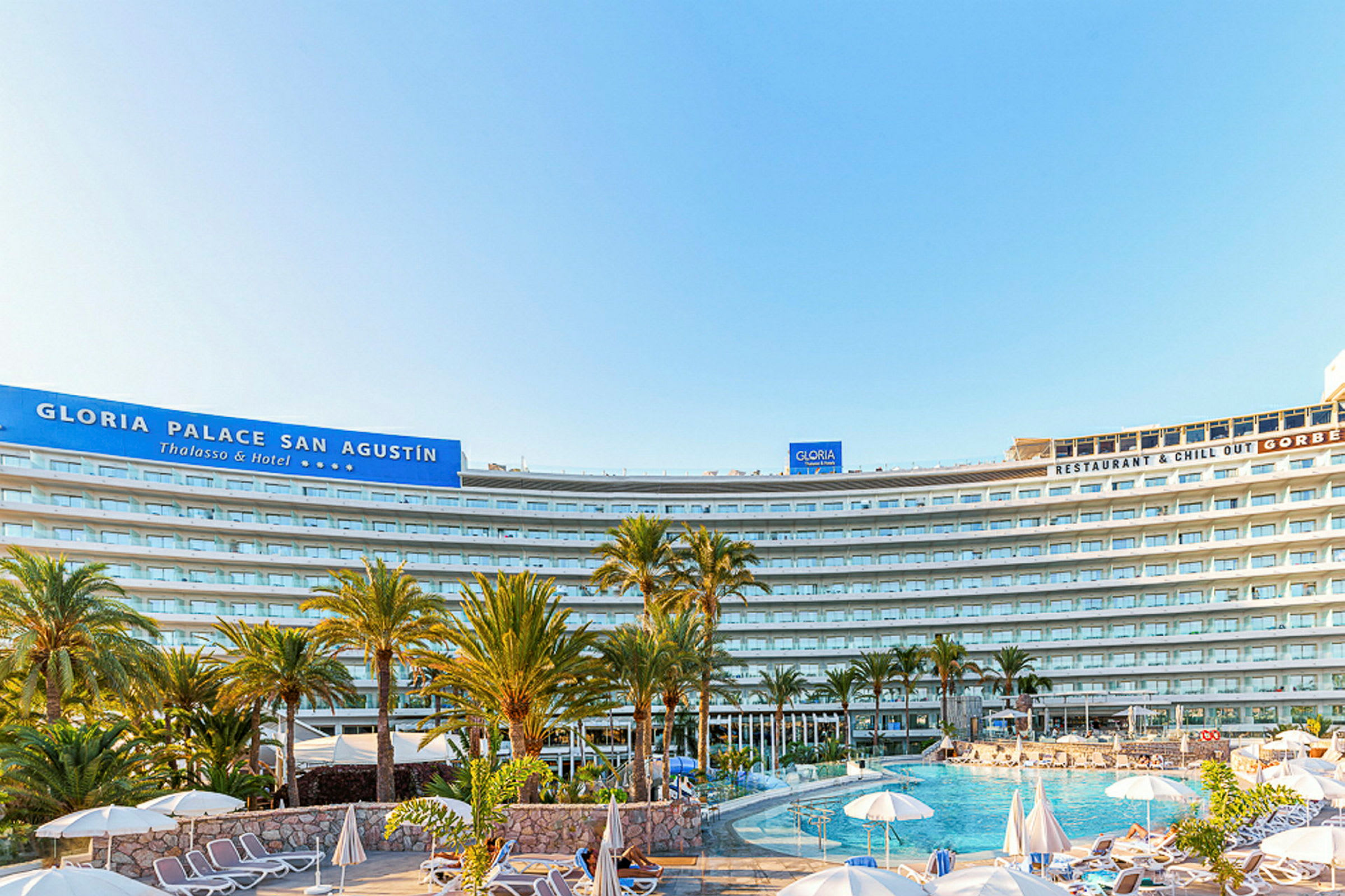 Bilde av hotellet Gloria Palace San Agustín med basseng og solsenger i forgrunnen. (AI-generert tekst)