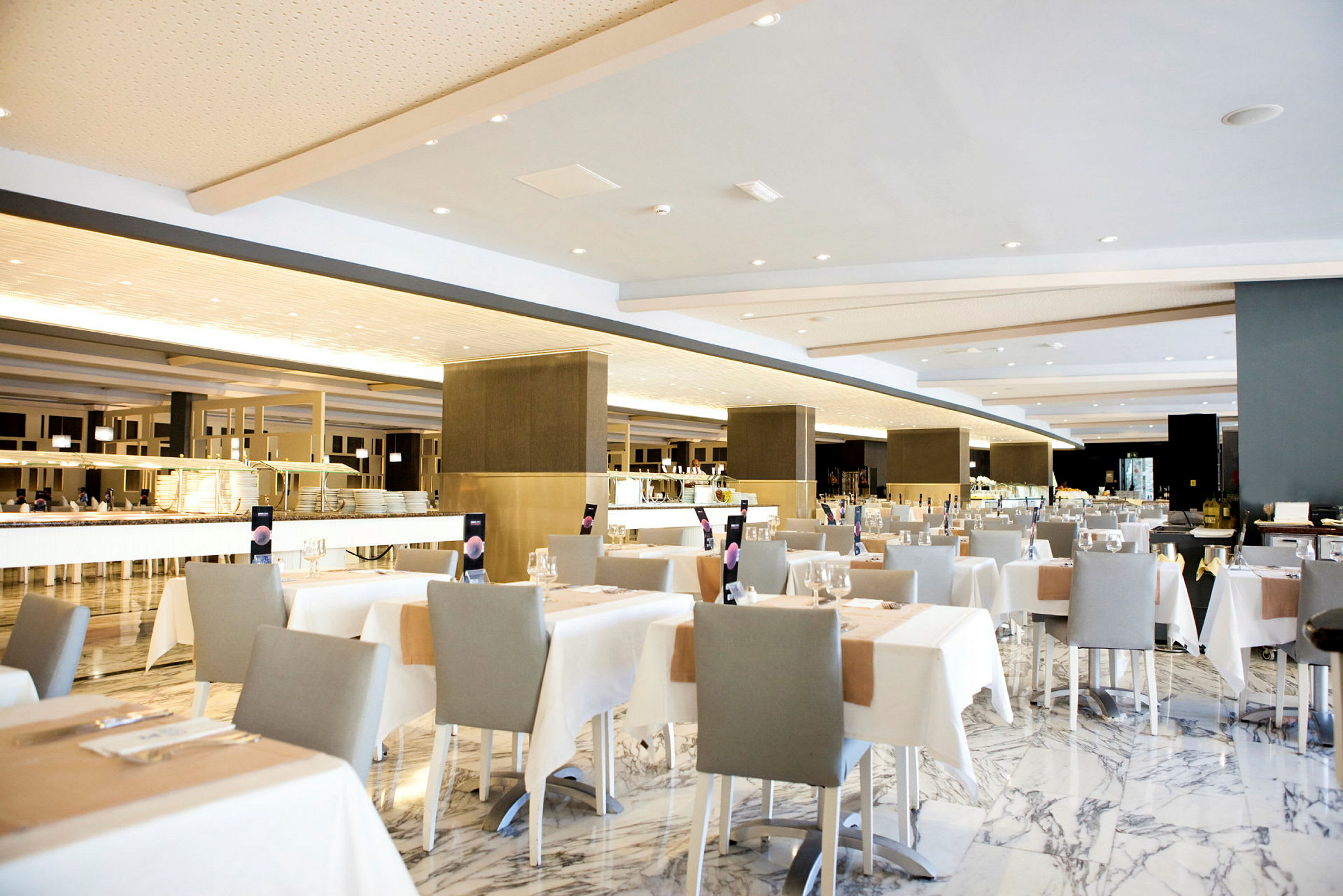 En romslig restaurant med elegante oppsatte bord, hvite duker og grå stoler. (AI-generert tekst)