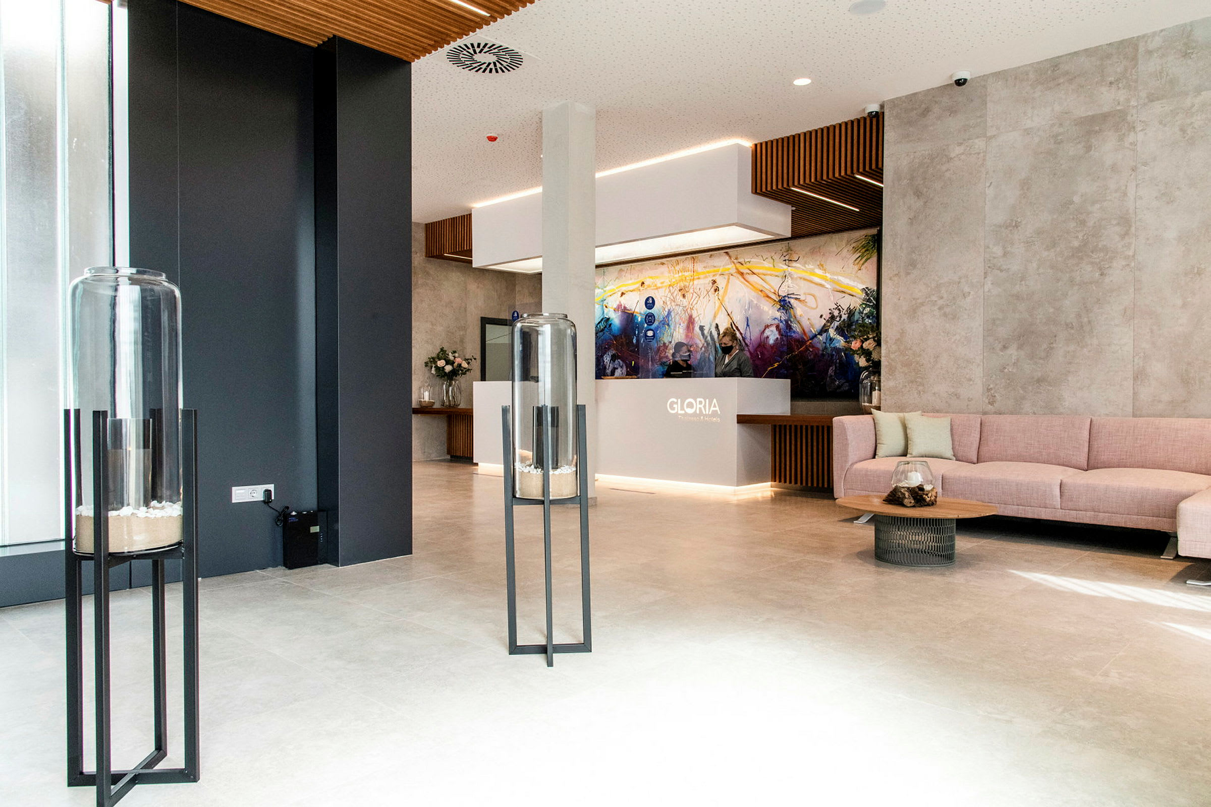 Moderne hotellobby med resepsjonen merket 'Gloria', sittemøbler og dekorative elementer som glassbeholdere på stativ. (AI-generert tekst)