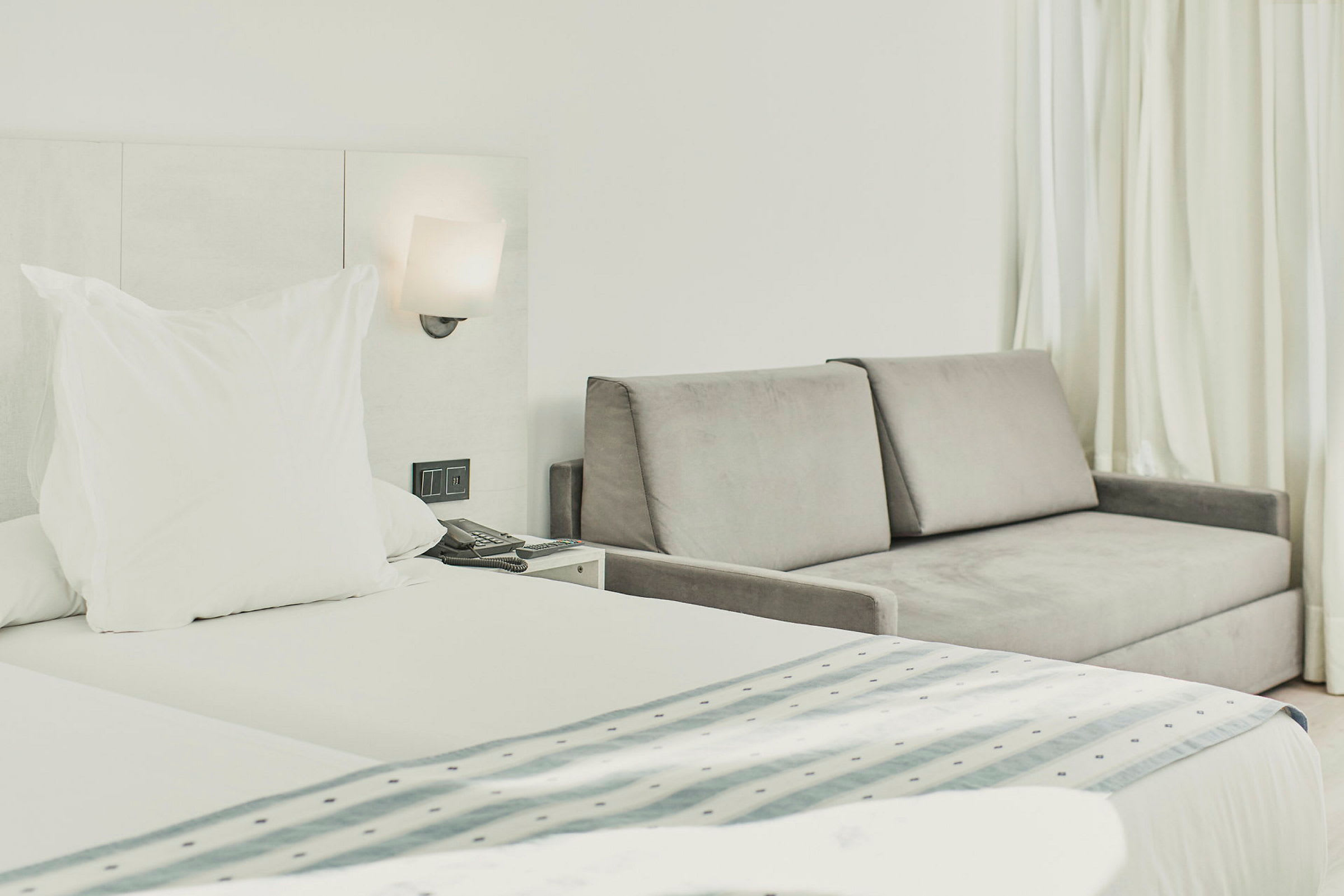 Hotellrom med seng og grå sofa ved siden av. (AI-generert tekst)