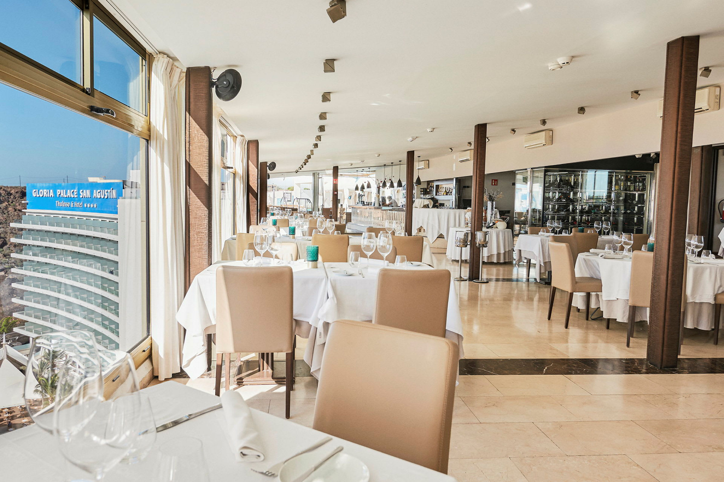 Bilde av en restaurant med oppdekkede bord og stoler ved siden av store vinduer. (AI-generert tekst)