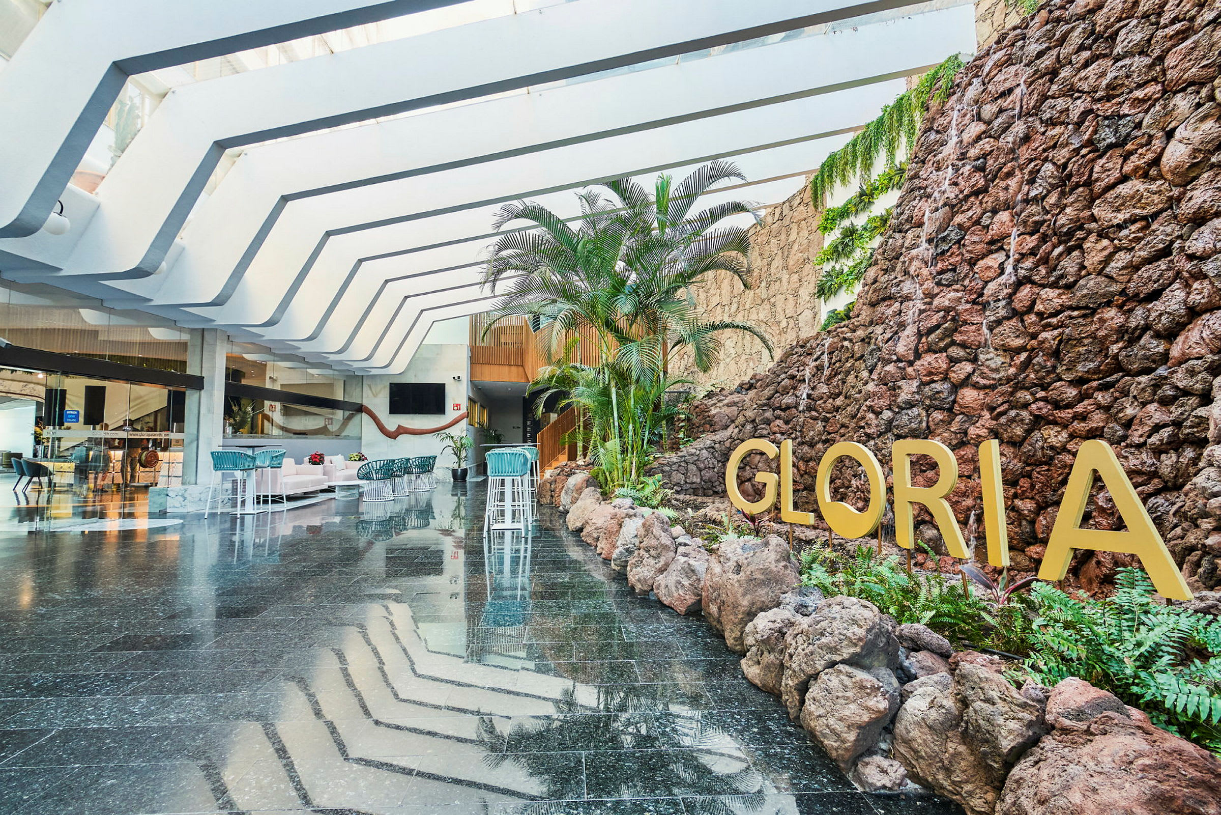 Hotellobby med steinvegg, planter og teksten Gloria. (AI-generert tekst)