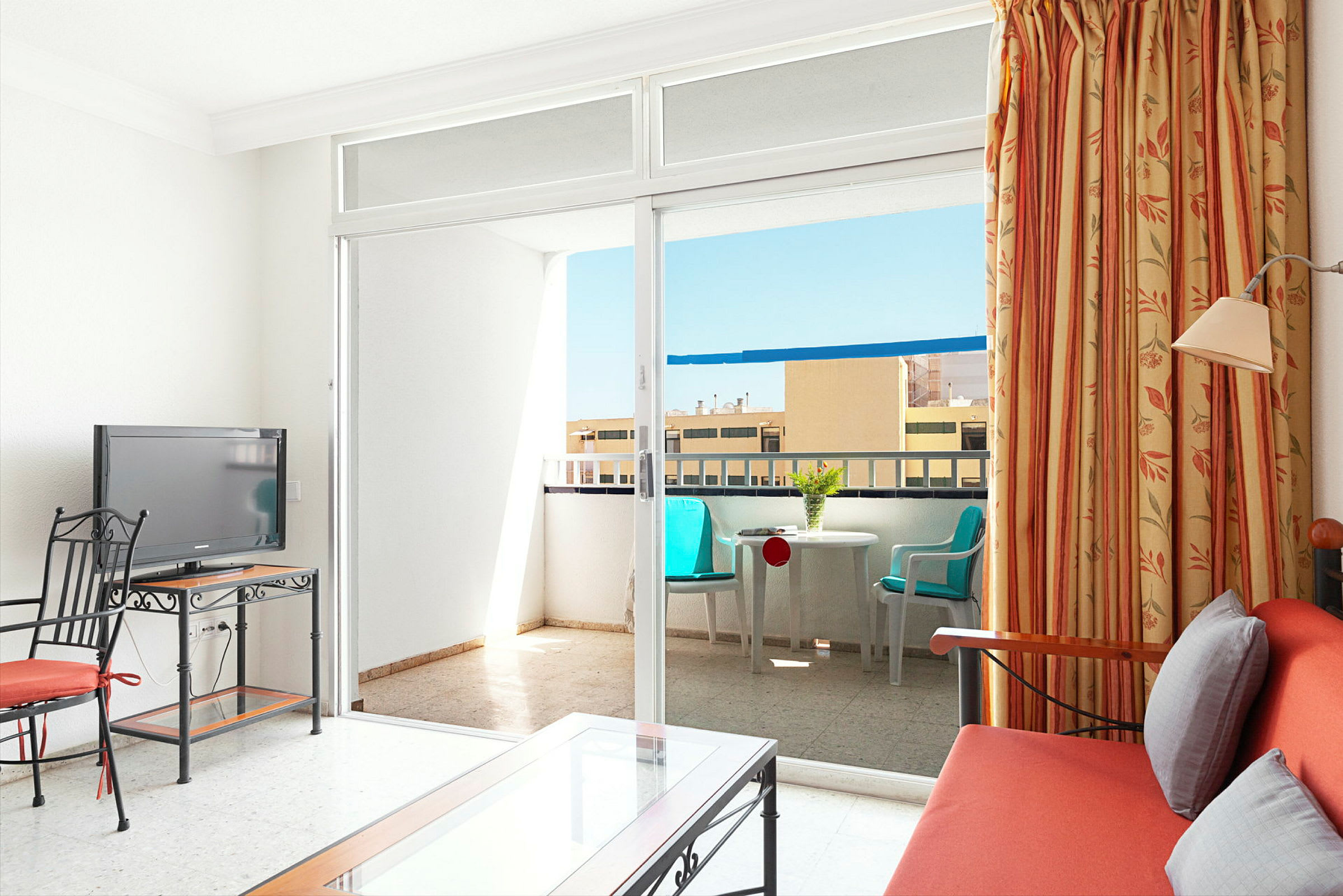 Et hotellrom med en sofa, en TV og et bord, samt en balkong med sittemøbler. (AI-generert tekst)