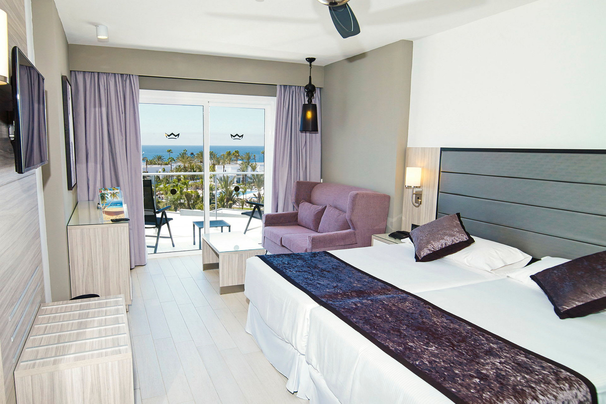 Moderne hotellrom med en dobbeltseng, sofagruppe og balkong med utsikt over havet. (AI-generert tekst)