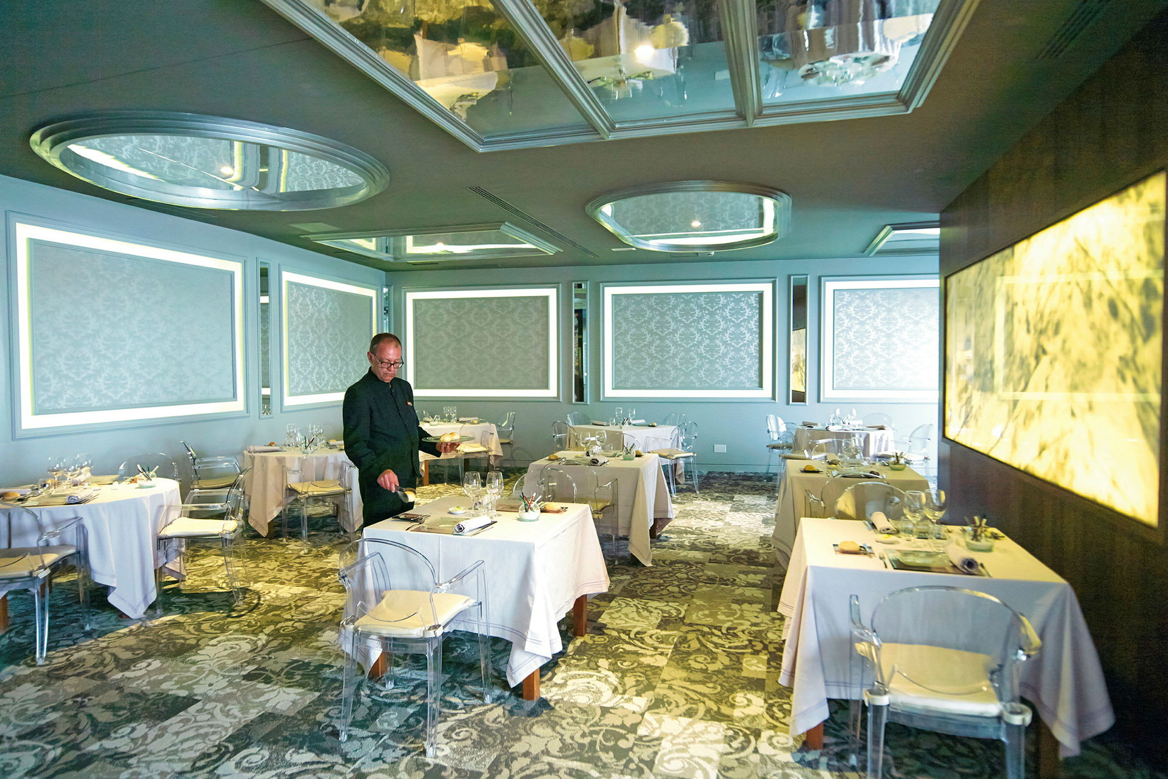 En elegant restaurant med bord dekket med hvite duker, mønstrede vegger og moderne lysinstallasjoner. (AI-generert tekst)