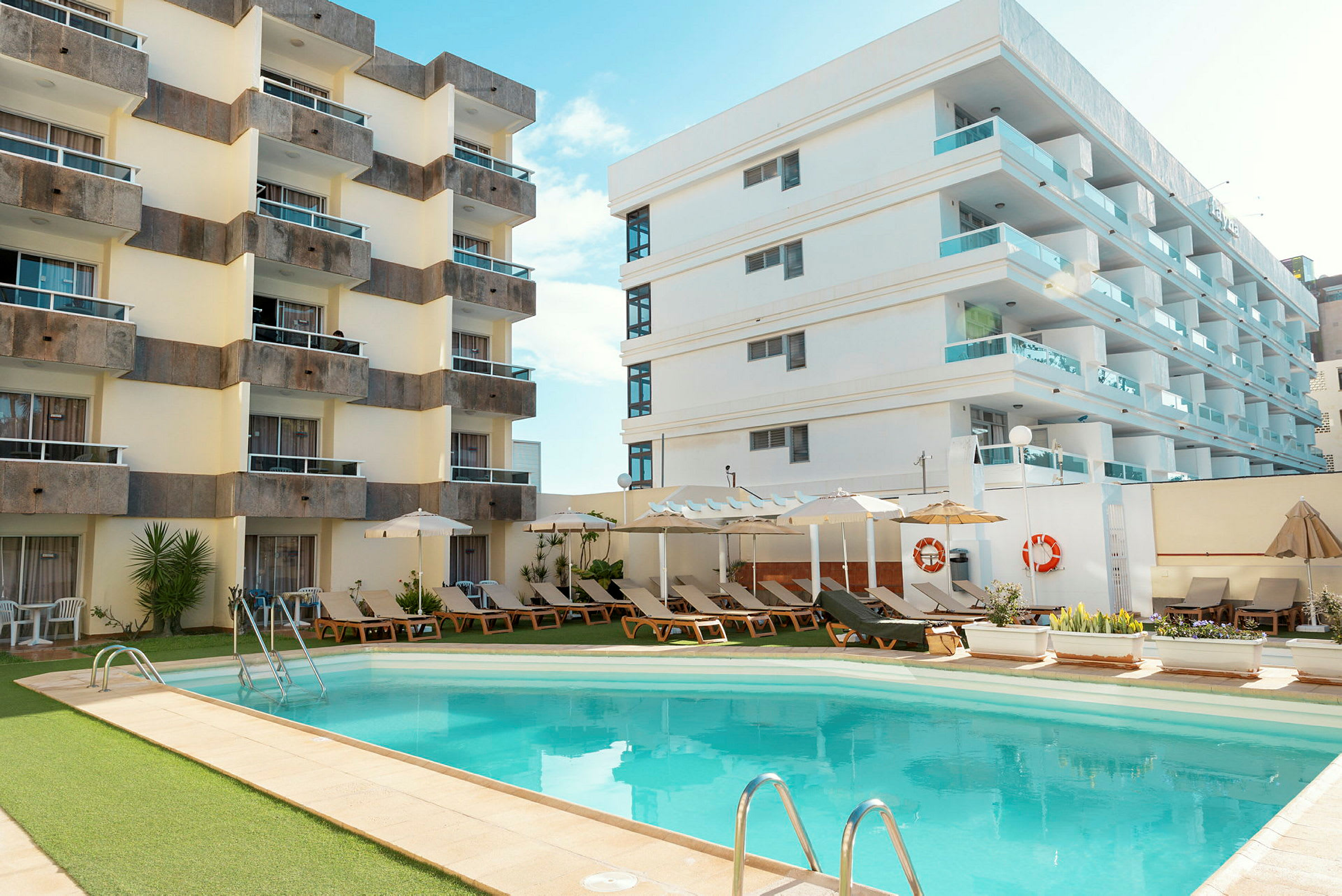 Hotellbygninger ved et utendørsbasseng omgitt av solsenger og parasoller. (AI-generert tekst)