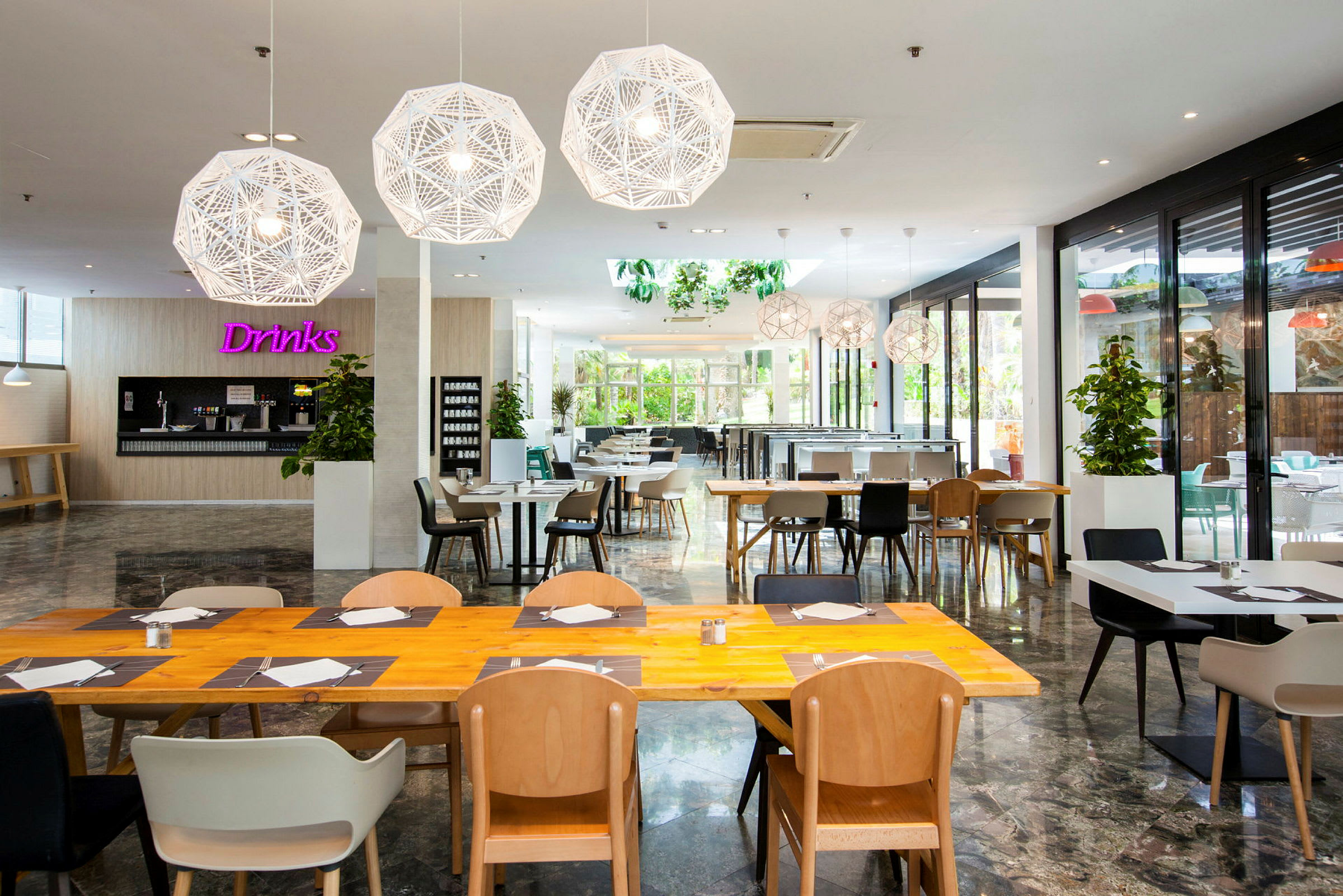 En lys og moderne restaurant med trebord og stoler, samt dekorative hengende lamper. (AI-generert tekst)