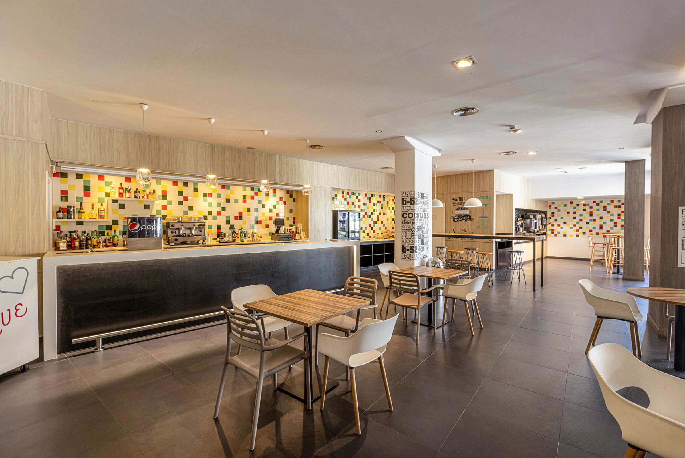Moderne kafé- og bardesign med fargerik flisvegg og møblerte bord og stoler. (AI-generert tekst)