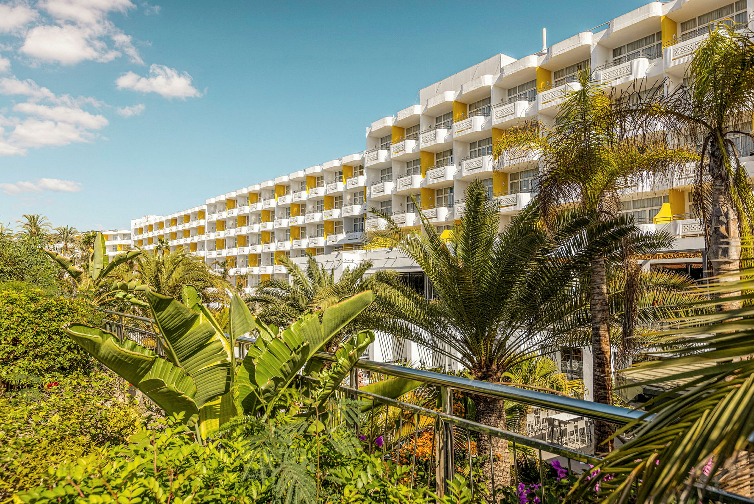 Flerårig hotell med gule balkonger omgitt av frodige palmer. (AI-generert tekst)