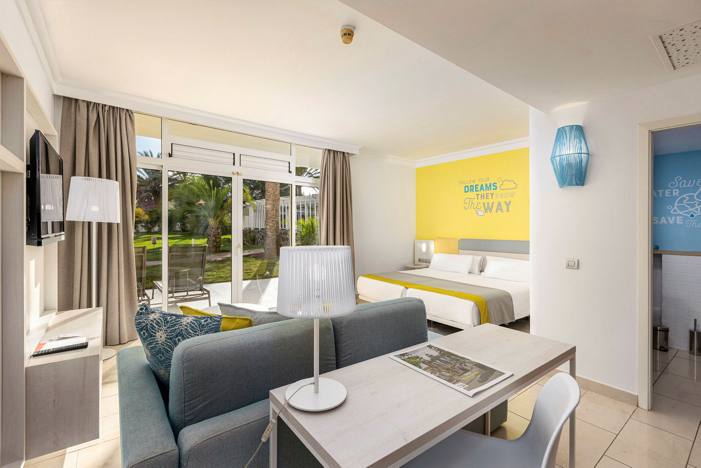 Moderne hotellrom med sittegruppe, seng og utsikt til hage. (AI-generert tekst)