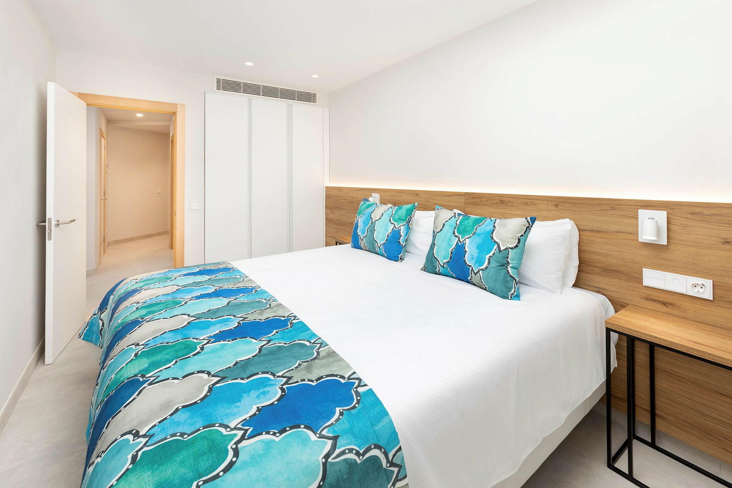 Seng med hvitt sengetøy og blå dekorative detaljer i et lyst hotellrom. (AI-generert tekst)