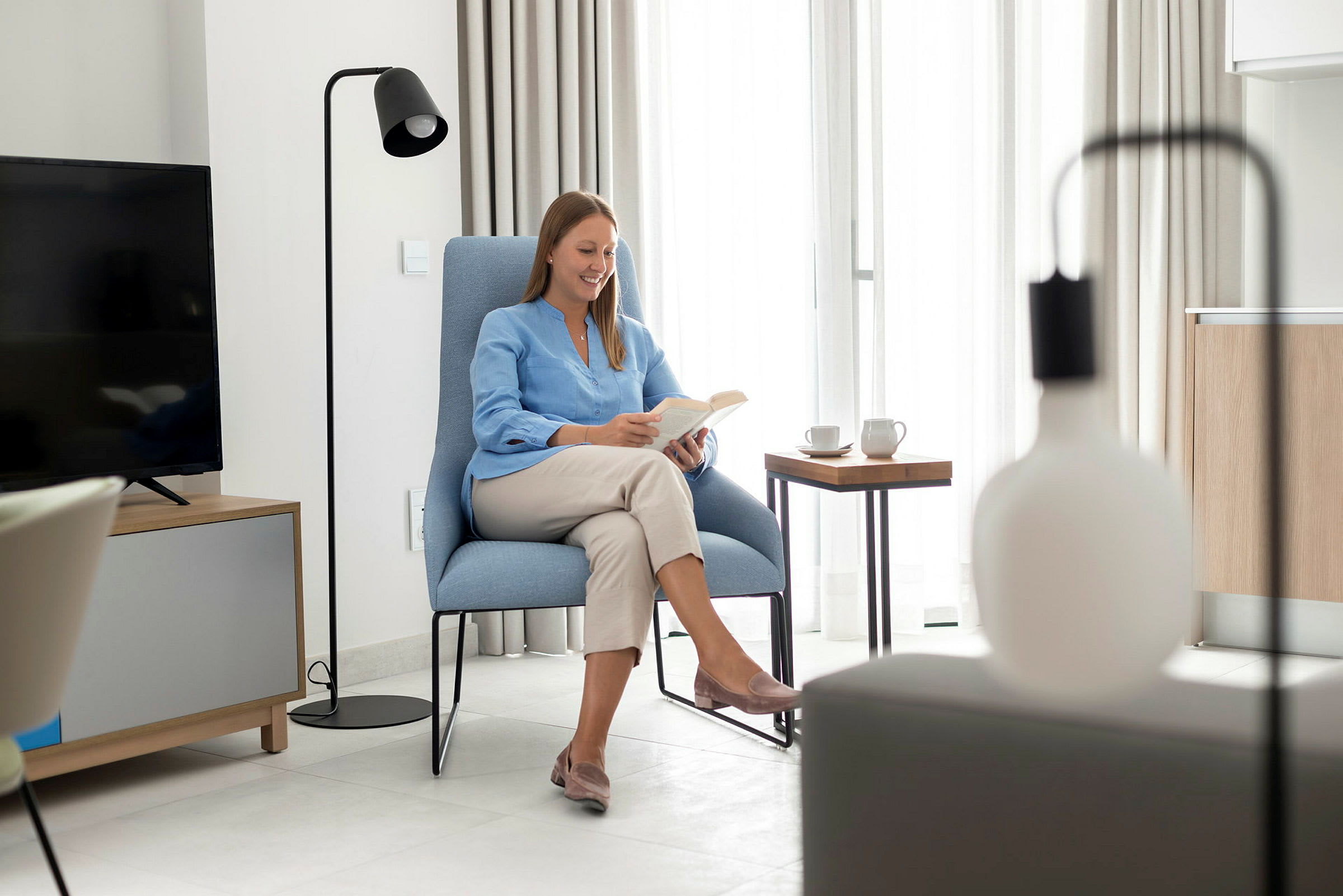 Moderne interiør med en person som sitter og leser i en solrik stue. (AI-generert tekst)