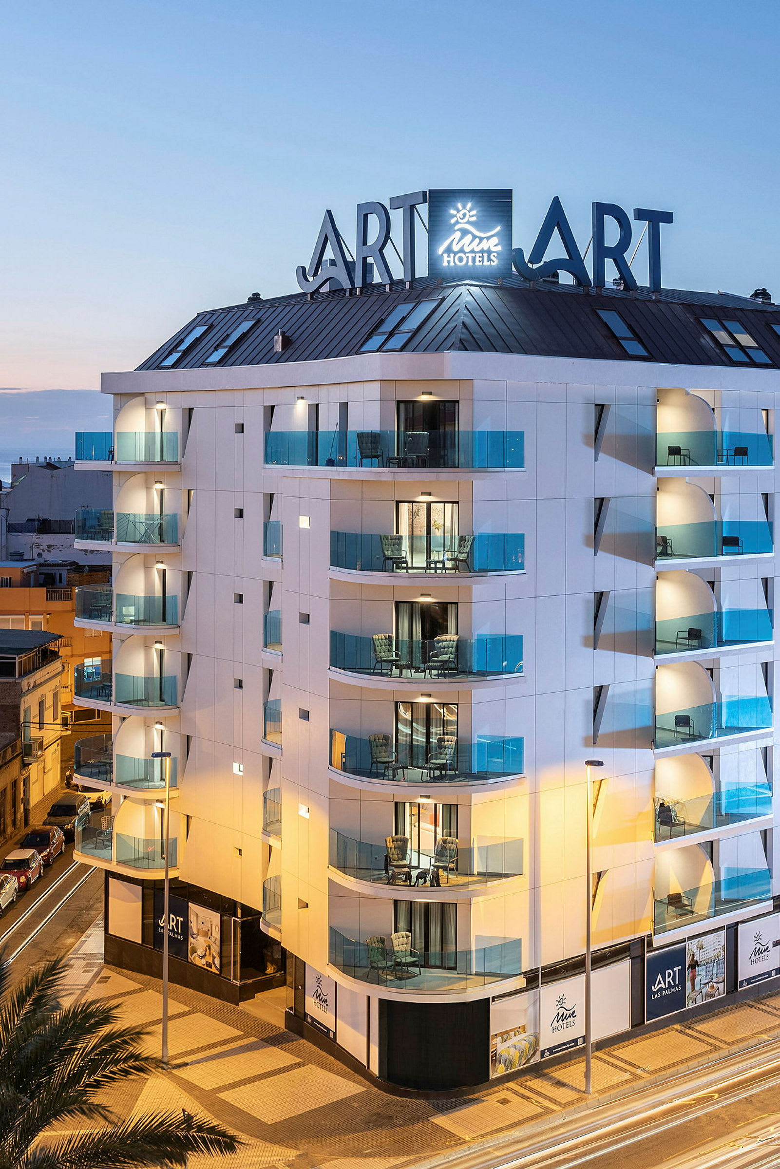 En moderne hotellbygning med glassbalkonger og skilt under en kveldshimmel. (AI-generert tekst)