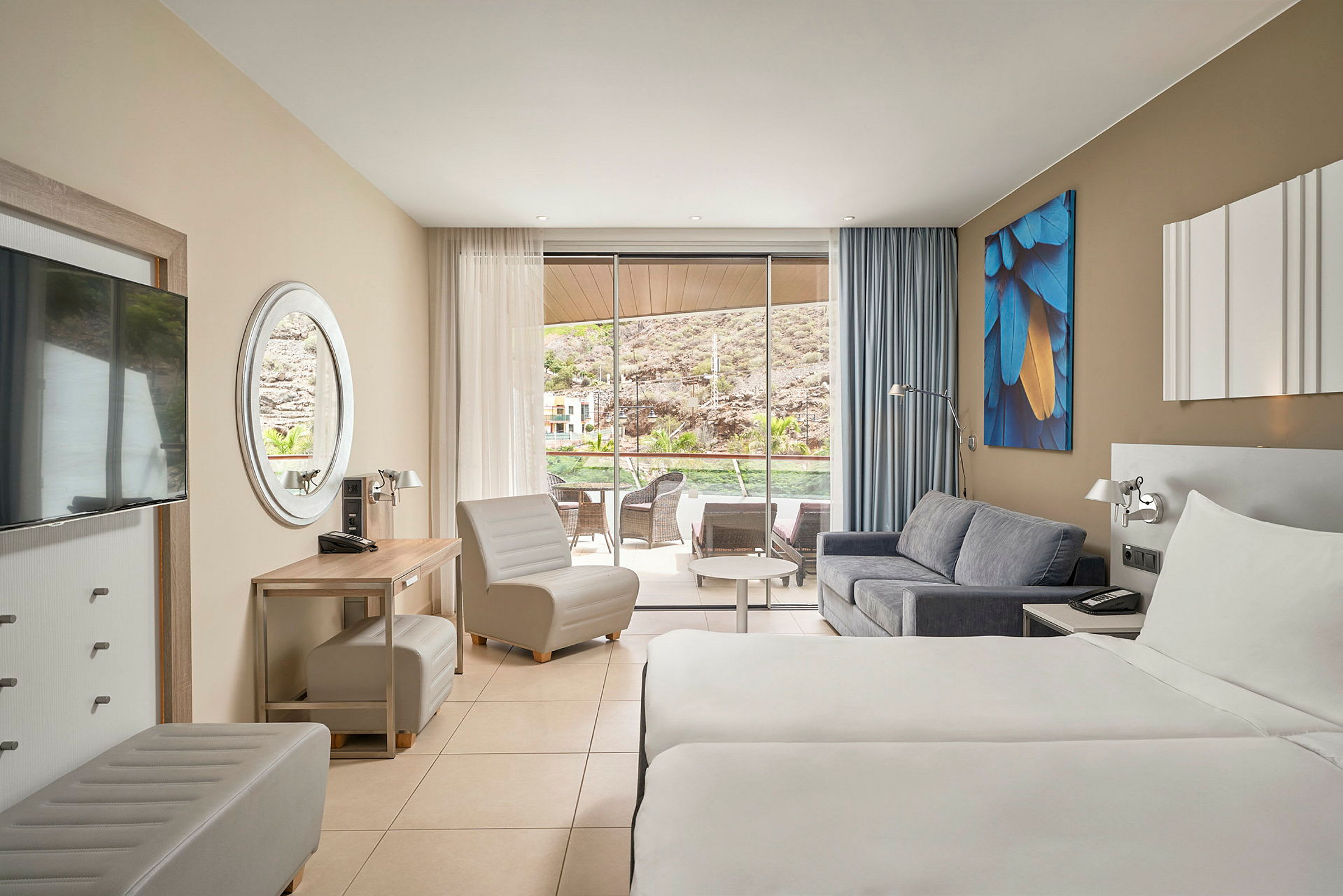 Hotellrom med to enkeltsenger, sofa og sittemøbler. Glasdører fører til en terrasse med utsikt. (AI-generert tekst)