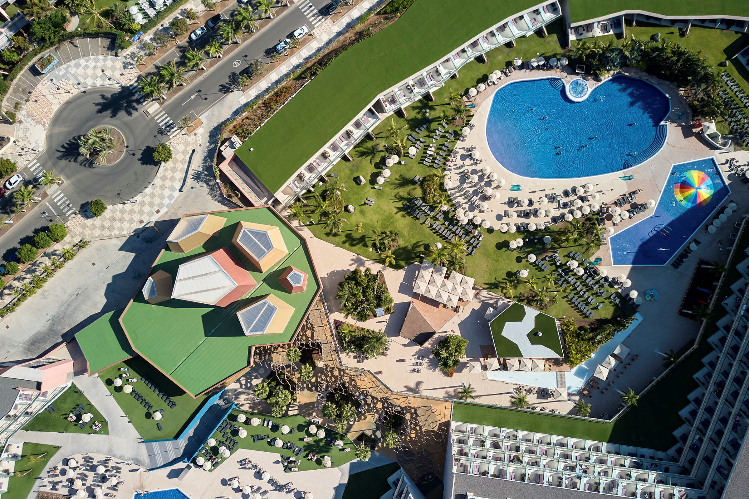 Flyfoto av en resort med bassengområde, grøntområder og bygninger. (AI-generert tekst)