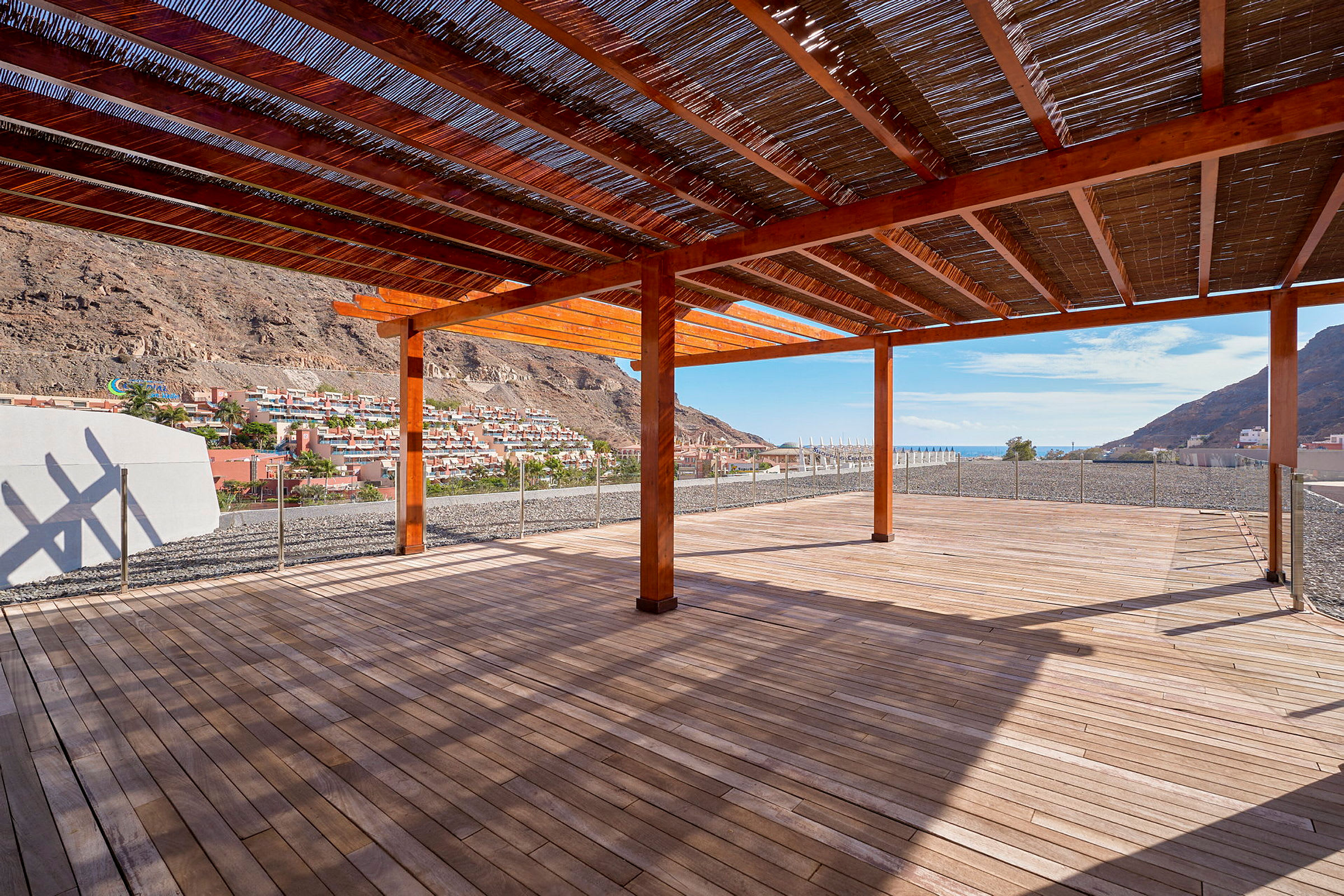 En pergola av tre med utsikt over en fjellskråning med hus og den blå himmelen i bakgrunnen. (AI-generert tekst)