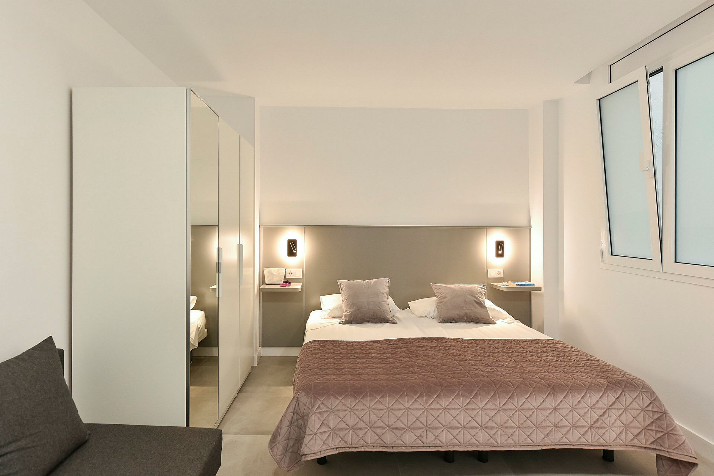 Et hotellrom med en dobbeltseng, et rosa sengeteppe og garderobe. (AI-generert tekst)