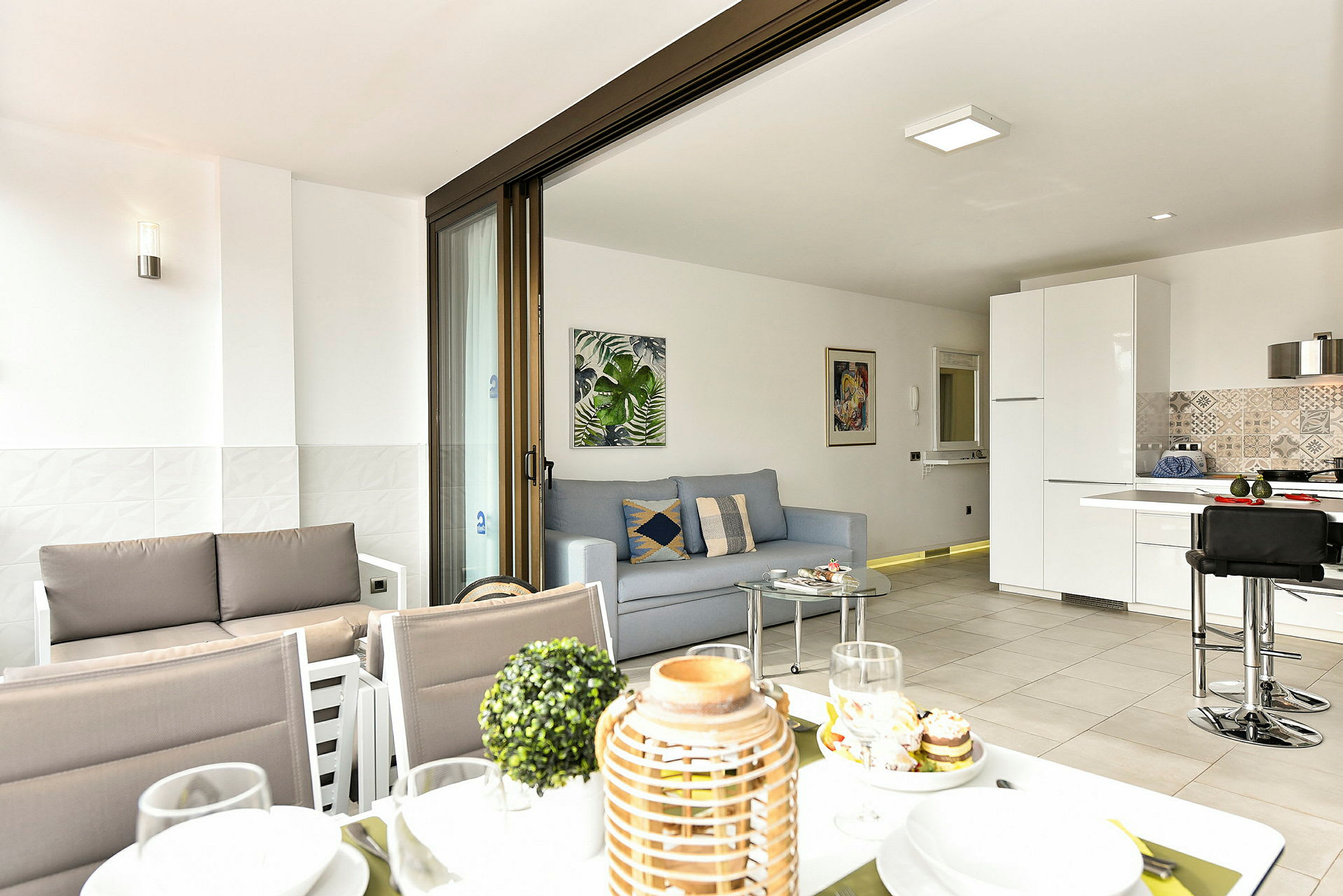 En moderne stue med åpen planløsning og kjøkken, synlig fra en terrasse med spiseplass. (AI-generert tekst)