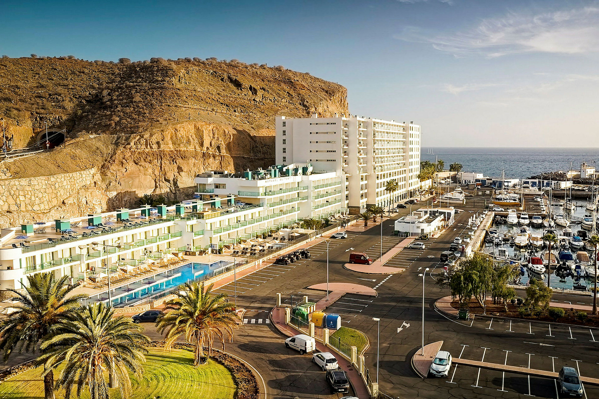 Hotell ved klippekant, med parkeringsplass og båthavn ved havet. (AI-generert tekst)