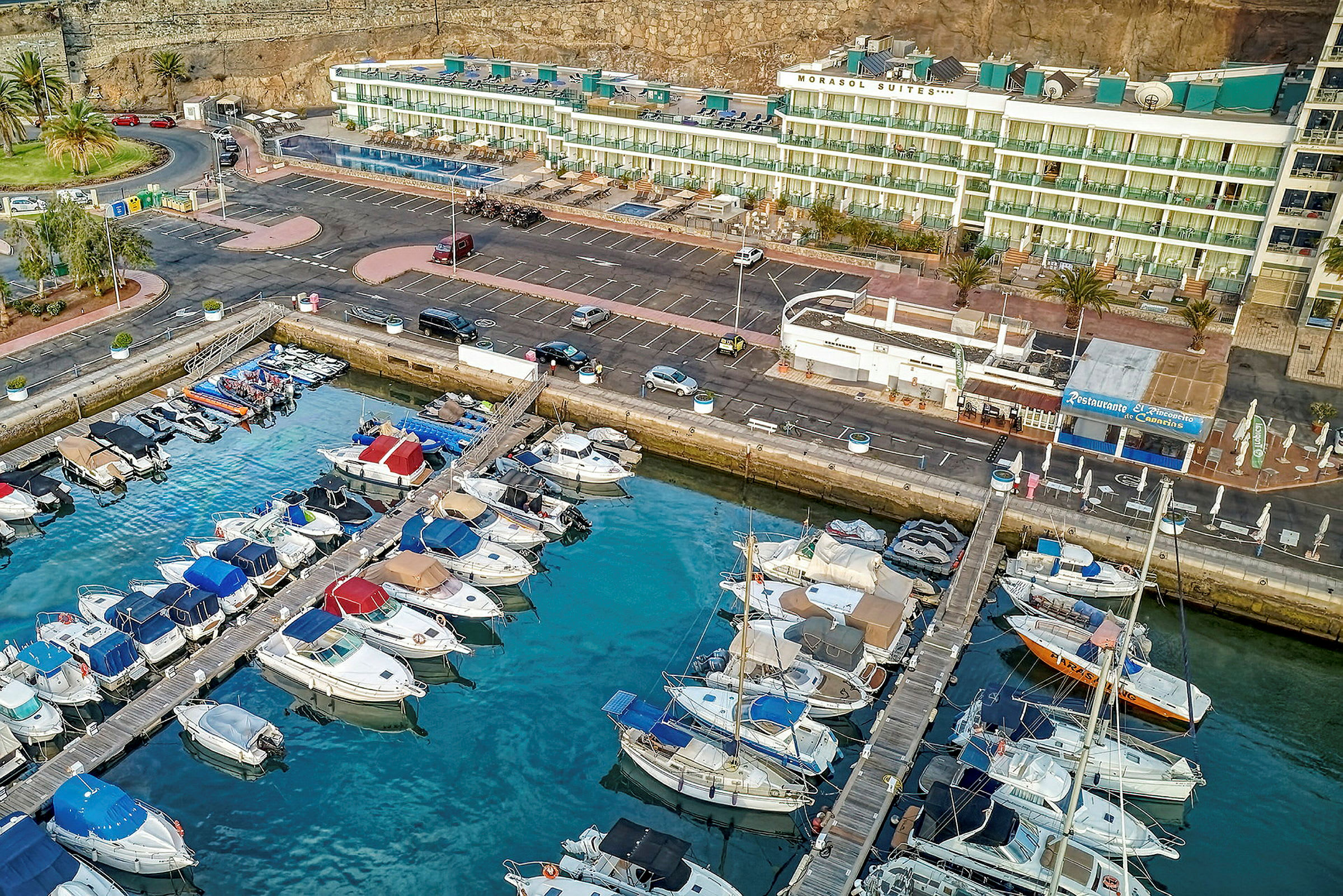 Luftfoto av en marina med parkerte båter foran bygninger og parkeringsplasser. (AI-generert tekst)
