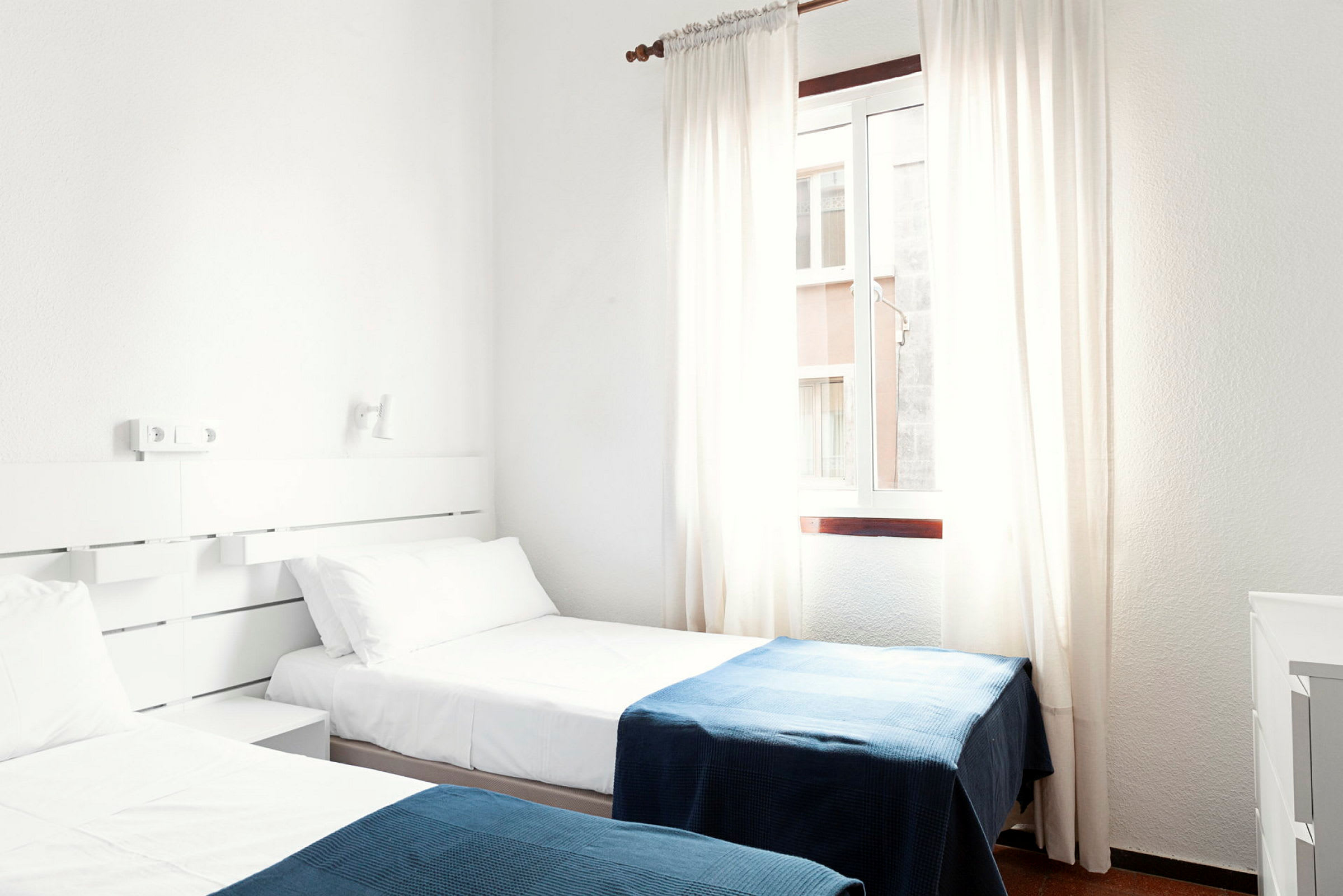 Et hotellrom med to enkeltsenger med hvite laken og blå tepper. (AI-generert tekst)