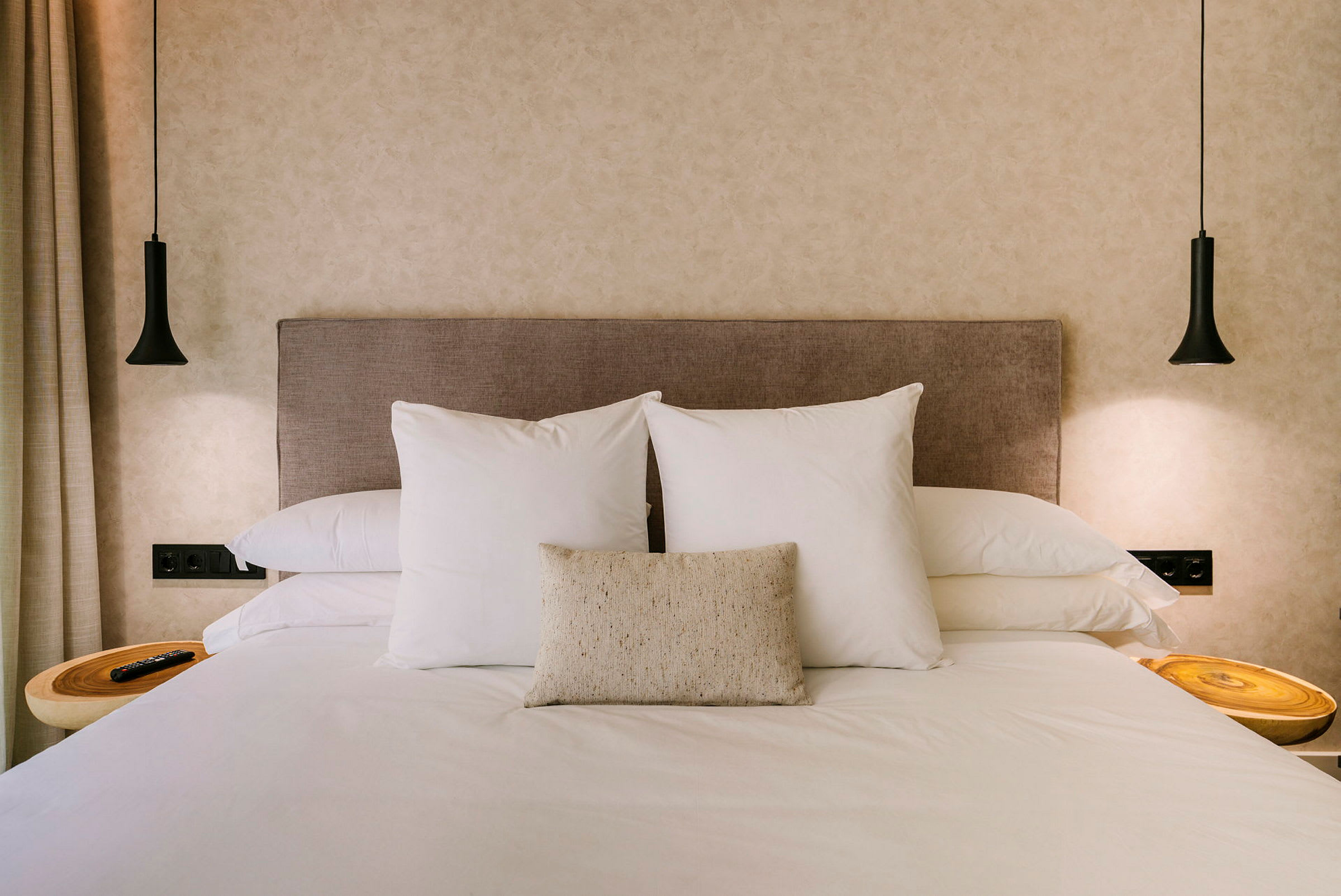 Hotellseng med to store hvite puter og en mindre pyntepute på beige hodegjerde. (AI-generert tekst)