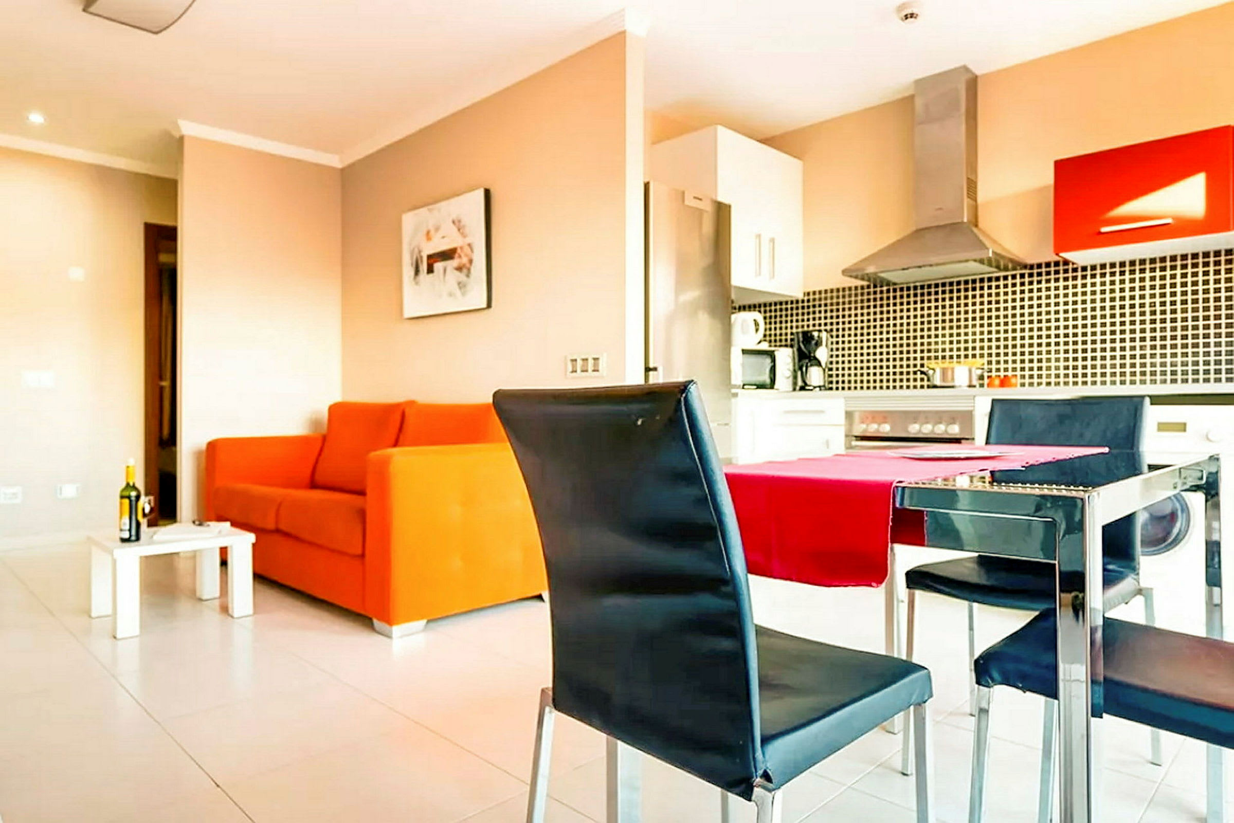 Stue med oransje sofa, spisebord og stoler, samt integrert kjøkken med komfyr og kjøkkenutstyr. (AI-generert tekst)