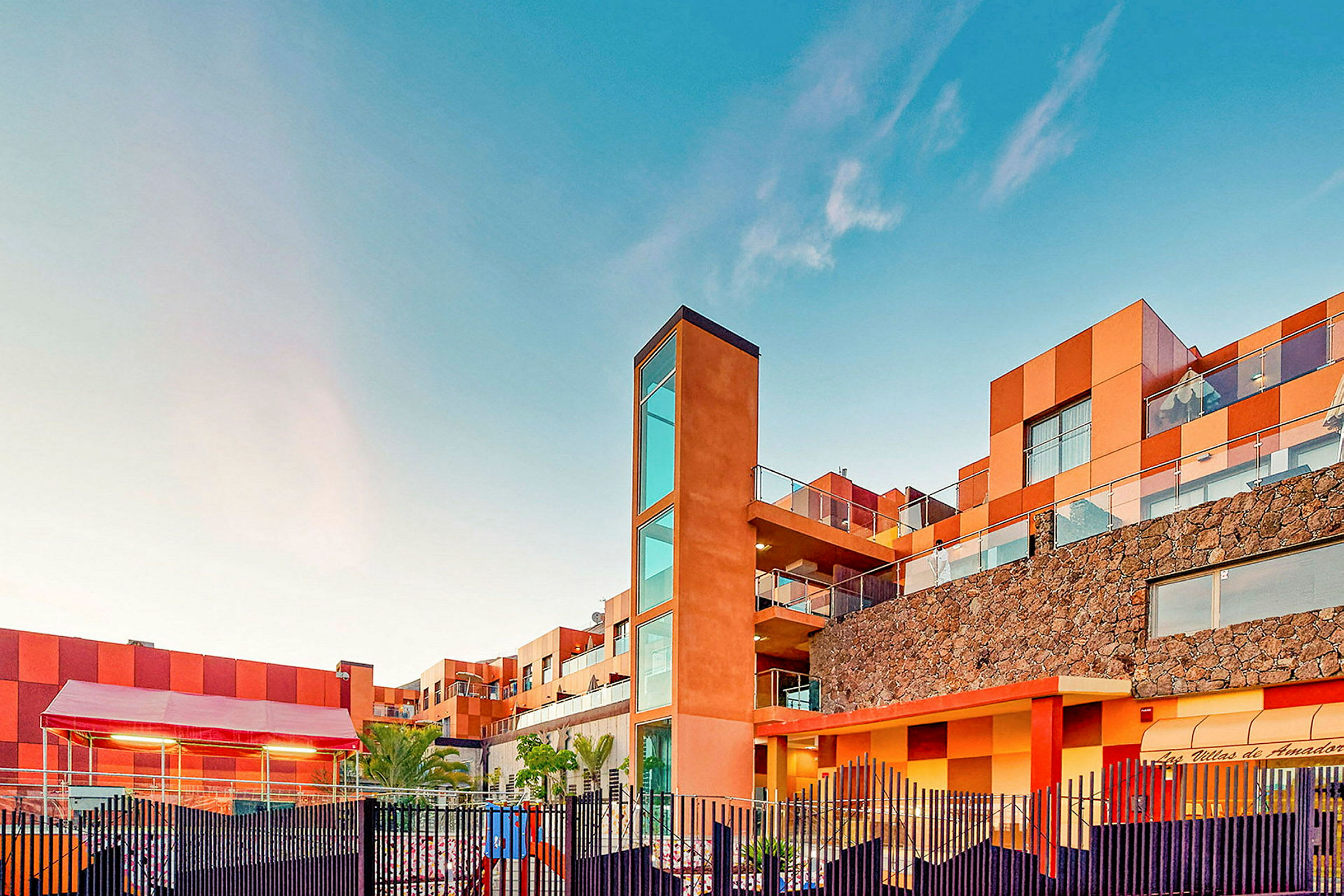 En bygning med moderne arkitektur og varme farger mot en klarblå himmel. (AI-generert tekst)