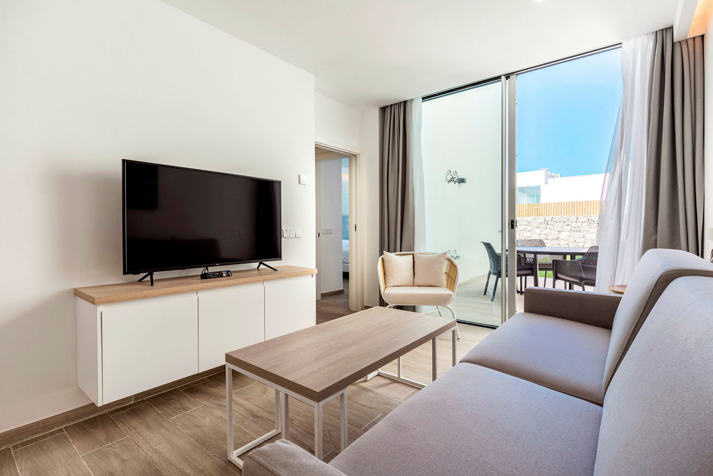 En moderne stue med sofa, sofabord, TV og vinduer som åpner seg til en terrasse. (AI-generert tekst)