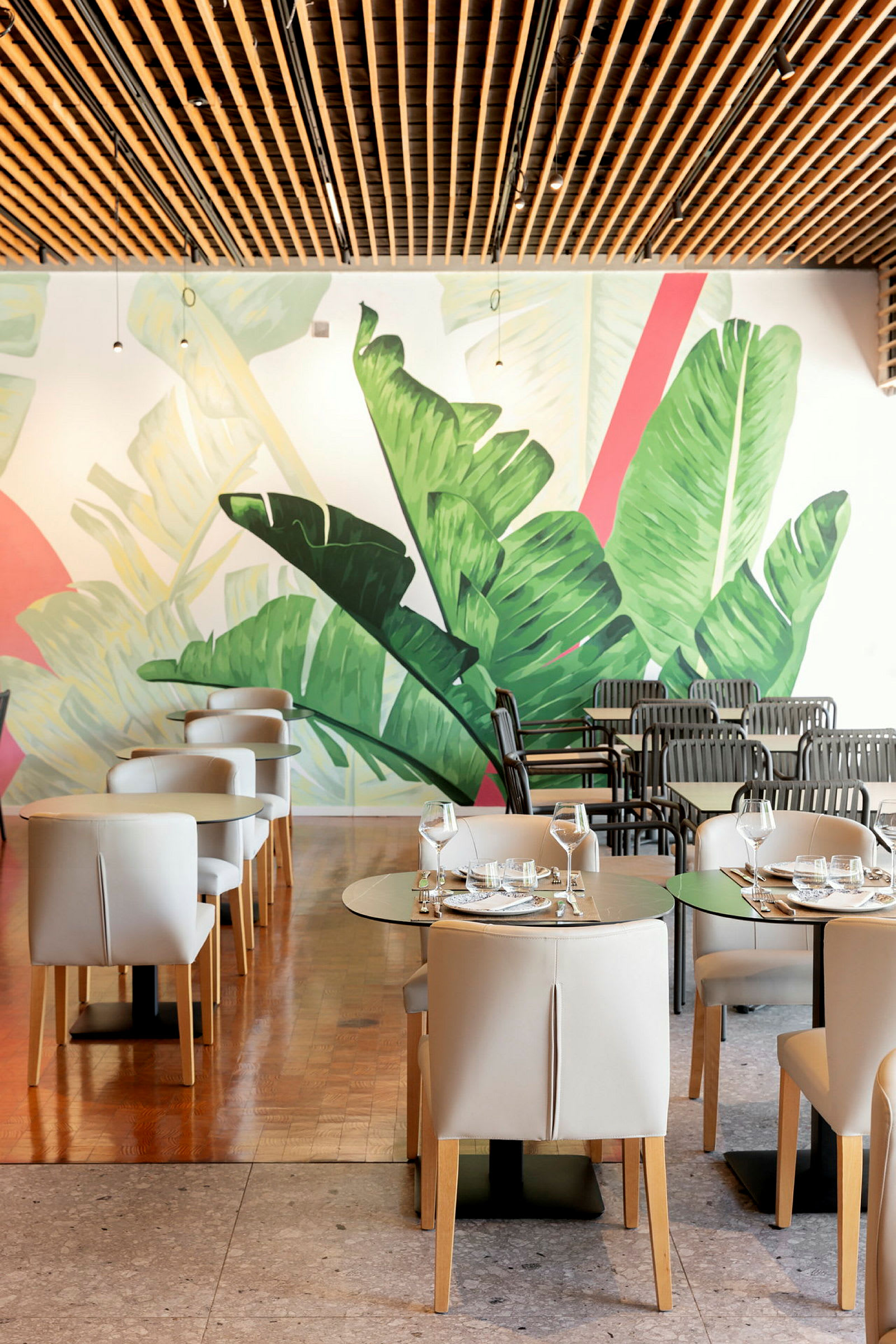 Restaurantmiljø med moderne møbler og en veggmaleri av store grønne blader. (AI-generert tekst)