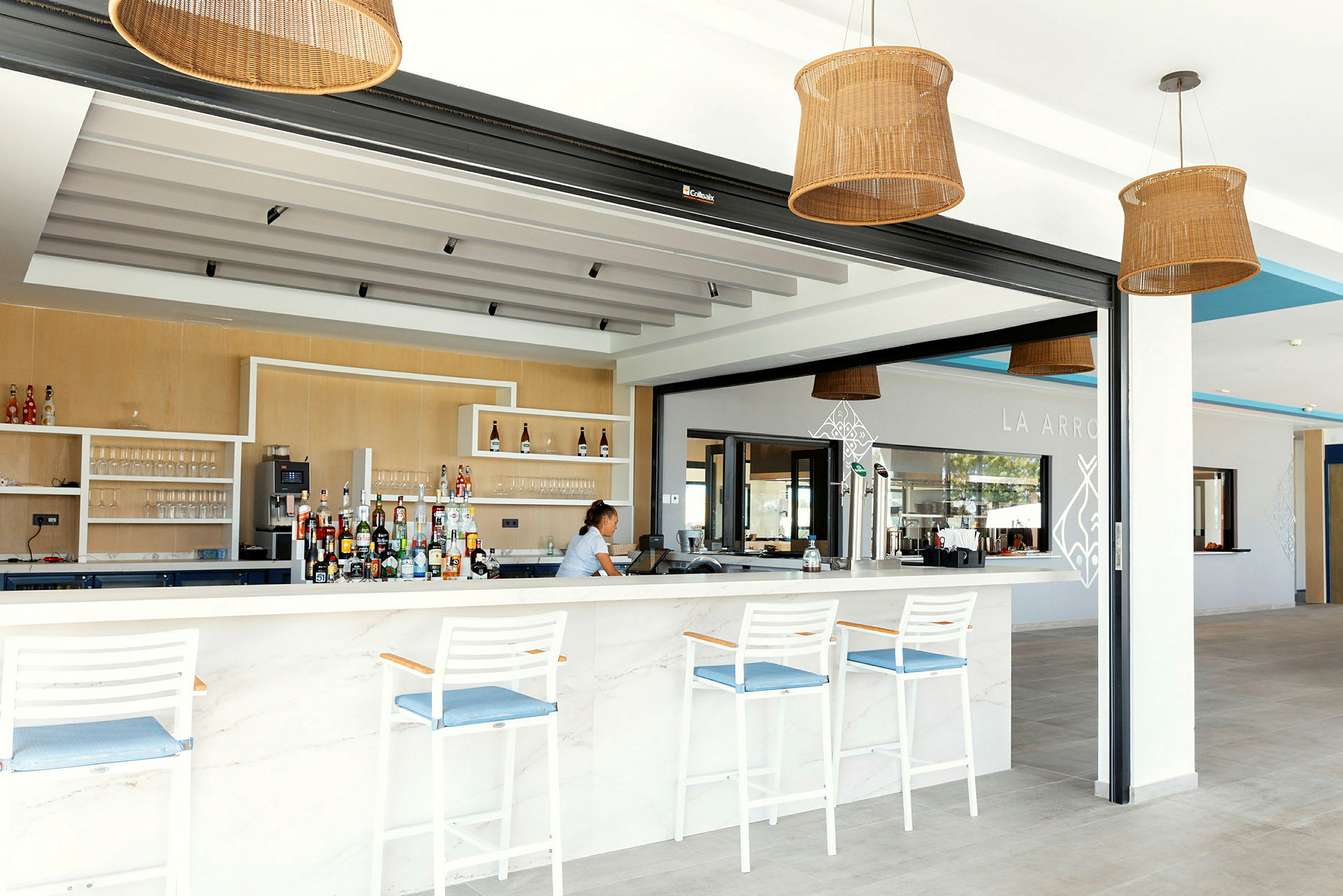 En elegant bar med hvit bardisk og blå detaljer, tre hvite barstoler og dekorative hengende lamper. (AI-generert tekst)