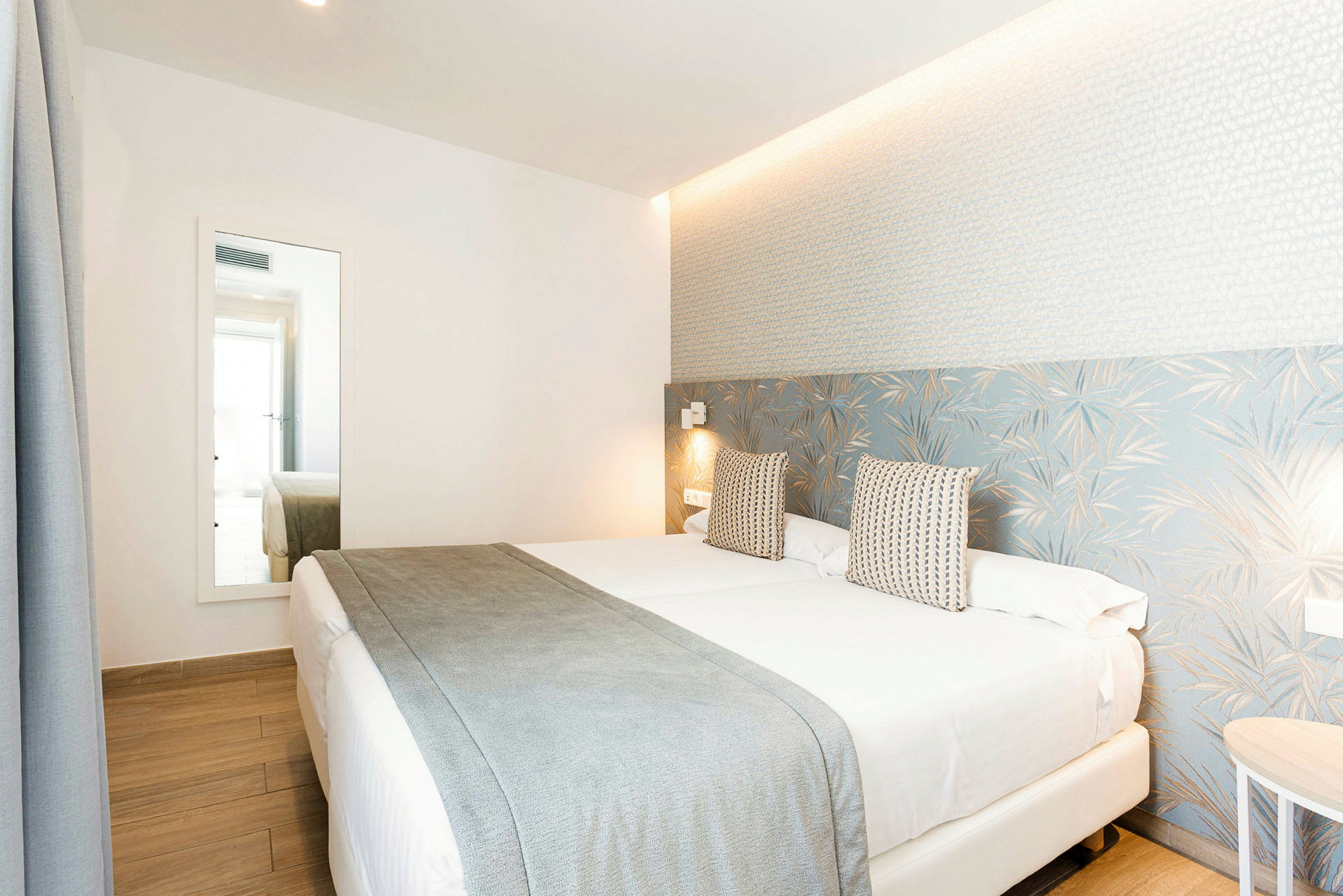 Hotellrom med en dobbeltseng, lys innredning og et stort speil. (AI-generert tekst)
