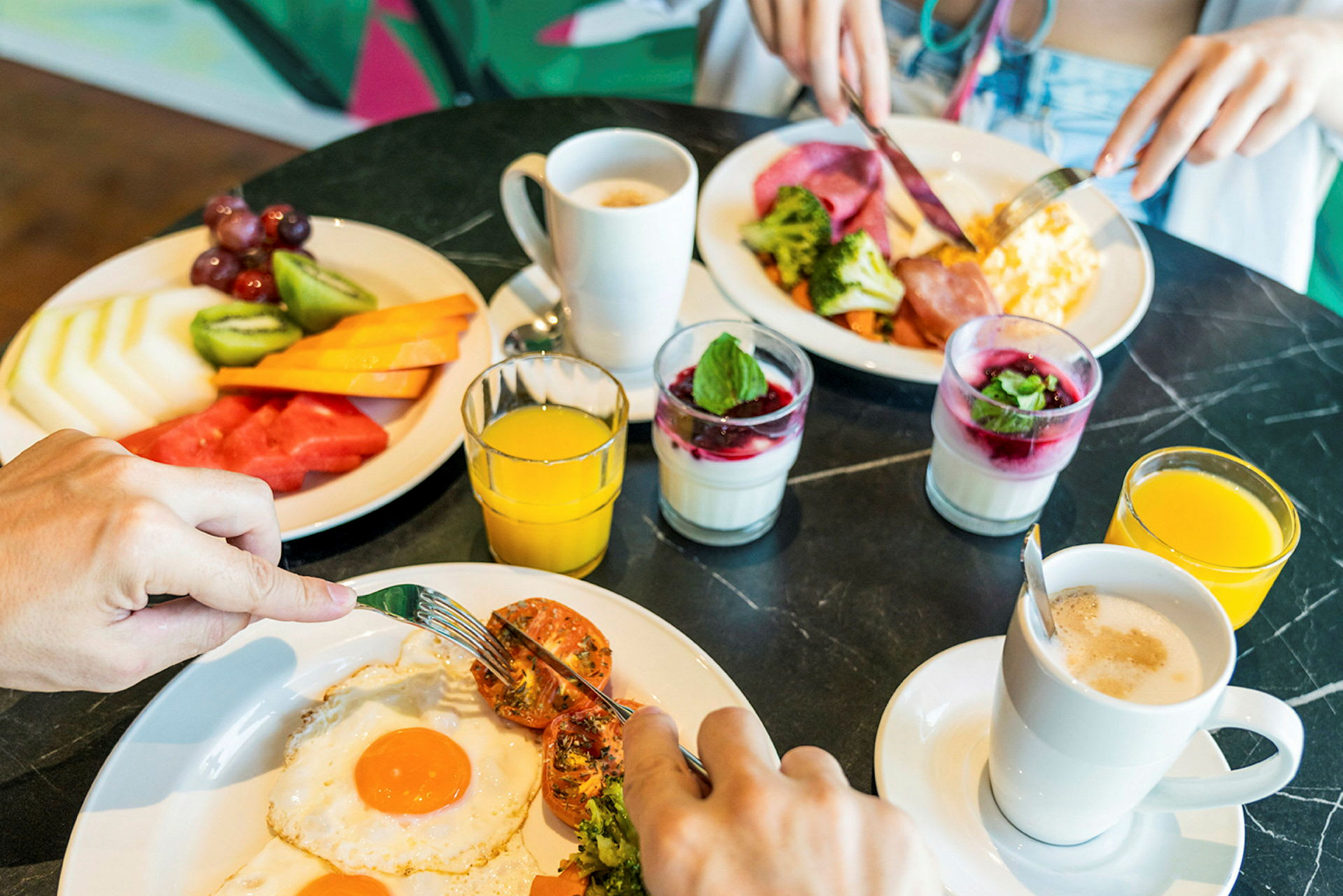 To tallerkener med frokostmat inkludert egg, frukt, brokkoli og kalde drikker. (AI-generert tekst)