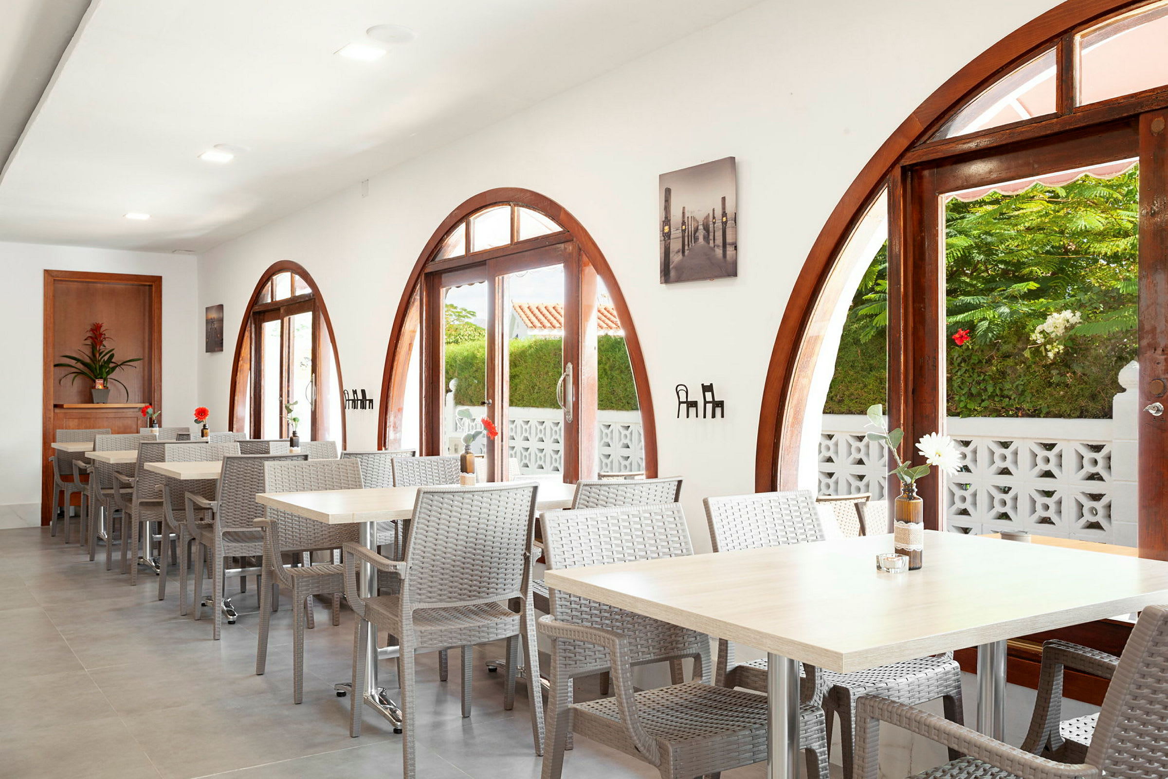 Restaurant med bueformede vinduer og bord med stoler. Planter utenfor vises gjennom vinduene. (AI-generert tekst)
