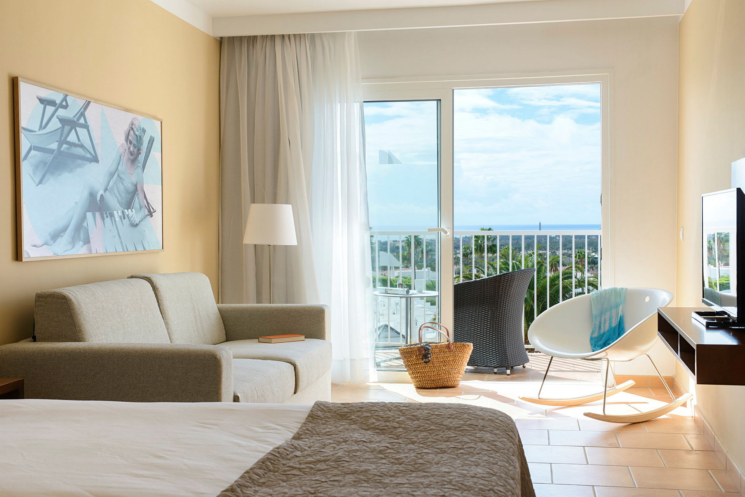 Et hotellrom med sofa, stol og balkong med utsikt over havet. (AI-generert tekst)