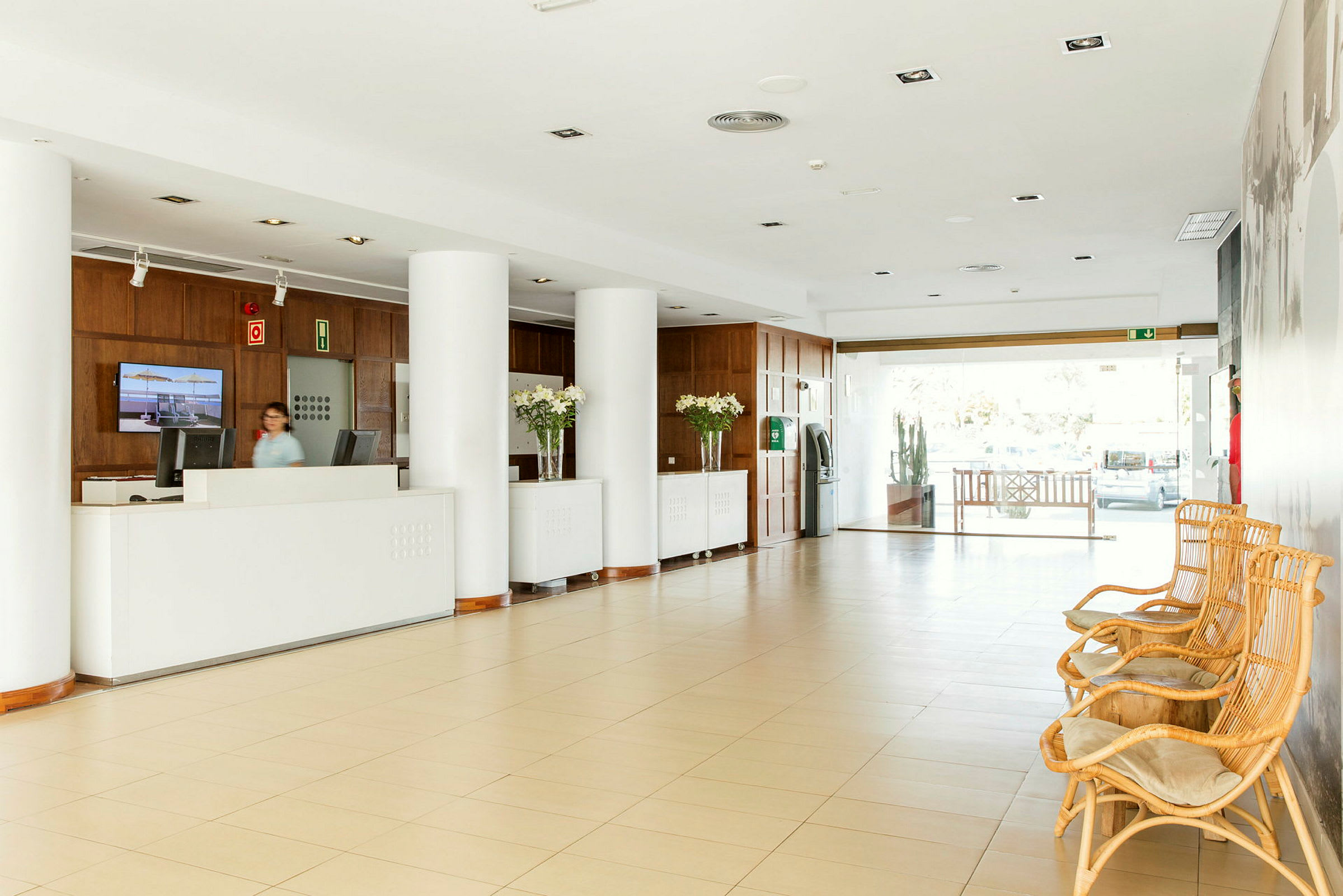 Hotellobby med resepsjon, store søyler og rottingmøbler. (AI-generert tekst)